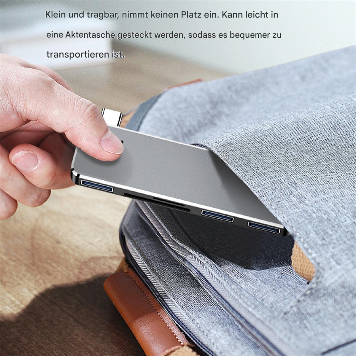 Eine Hand, die ein kleines silbernes Gerät hält, das teilweise in eine graue Tasche gesteckt wird.