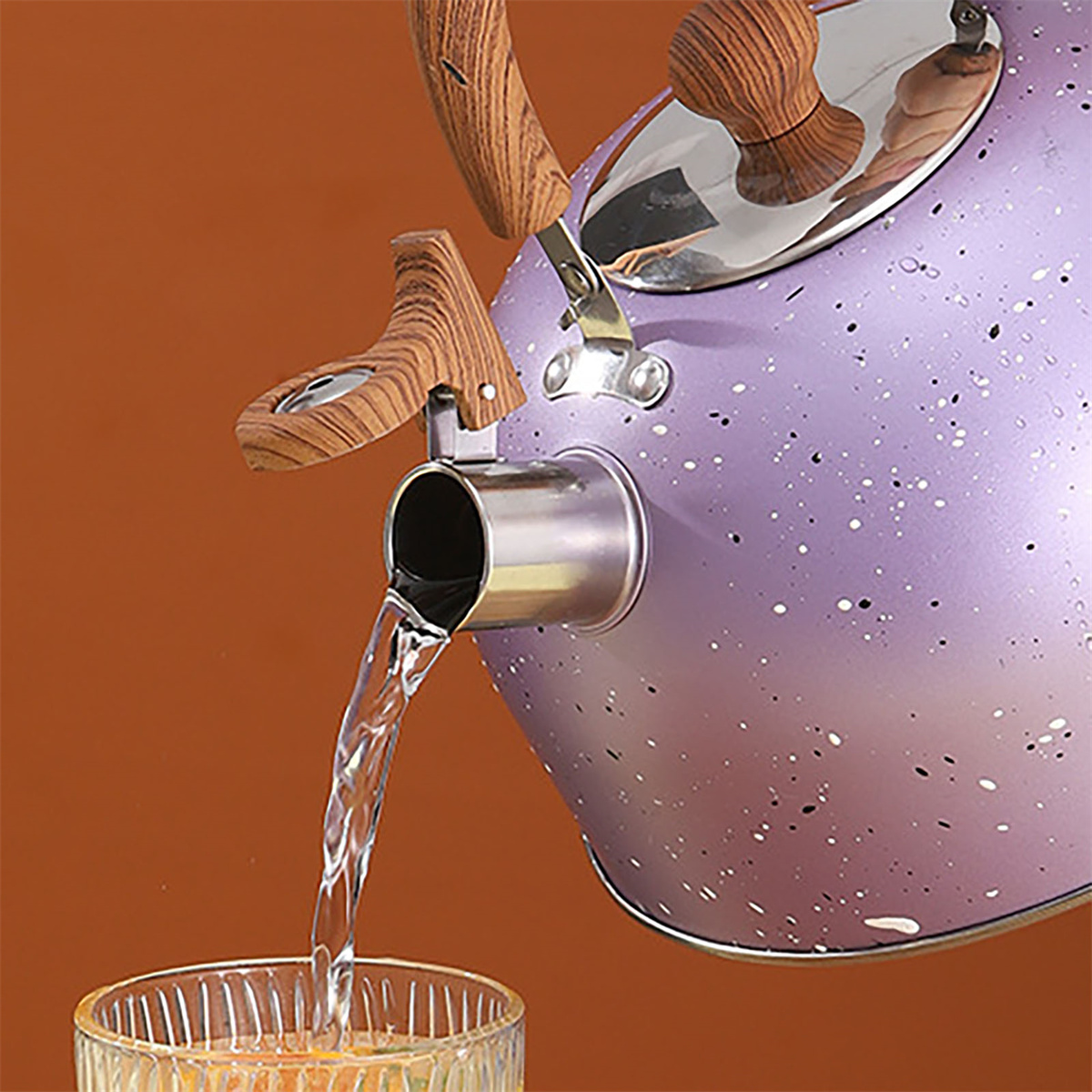Ein lila und weiß gesprenkelter Wasserkocher gießt Wasser in ein klares Glas.