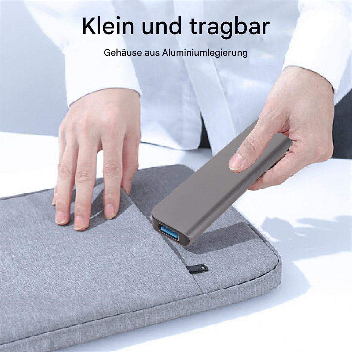 Hände halten einen grauen USB-Hub neben einer grauen Laptoptasche. Text: Klein und tragbar.