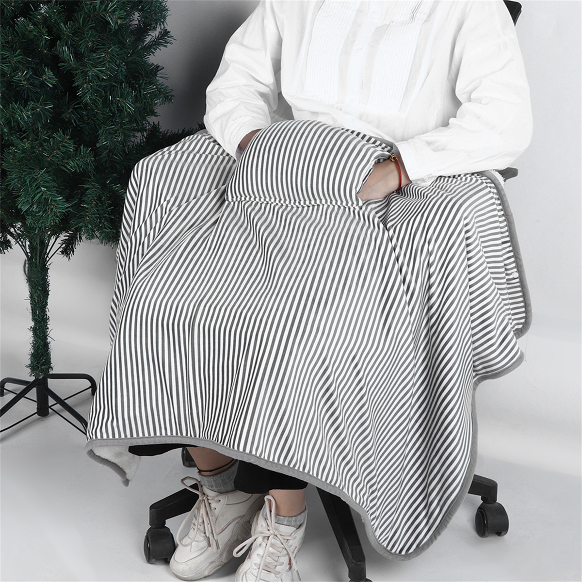Person, eingehüllt in eine gestreifte Decke auf einem Stuhl, in der Nähe eines Weihnachtsbaums.