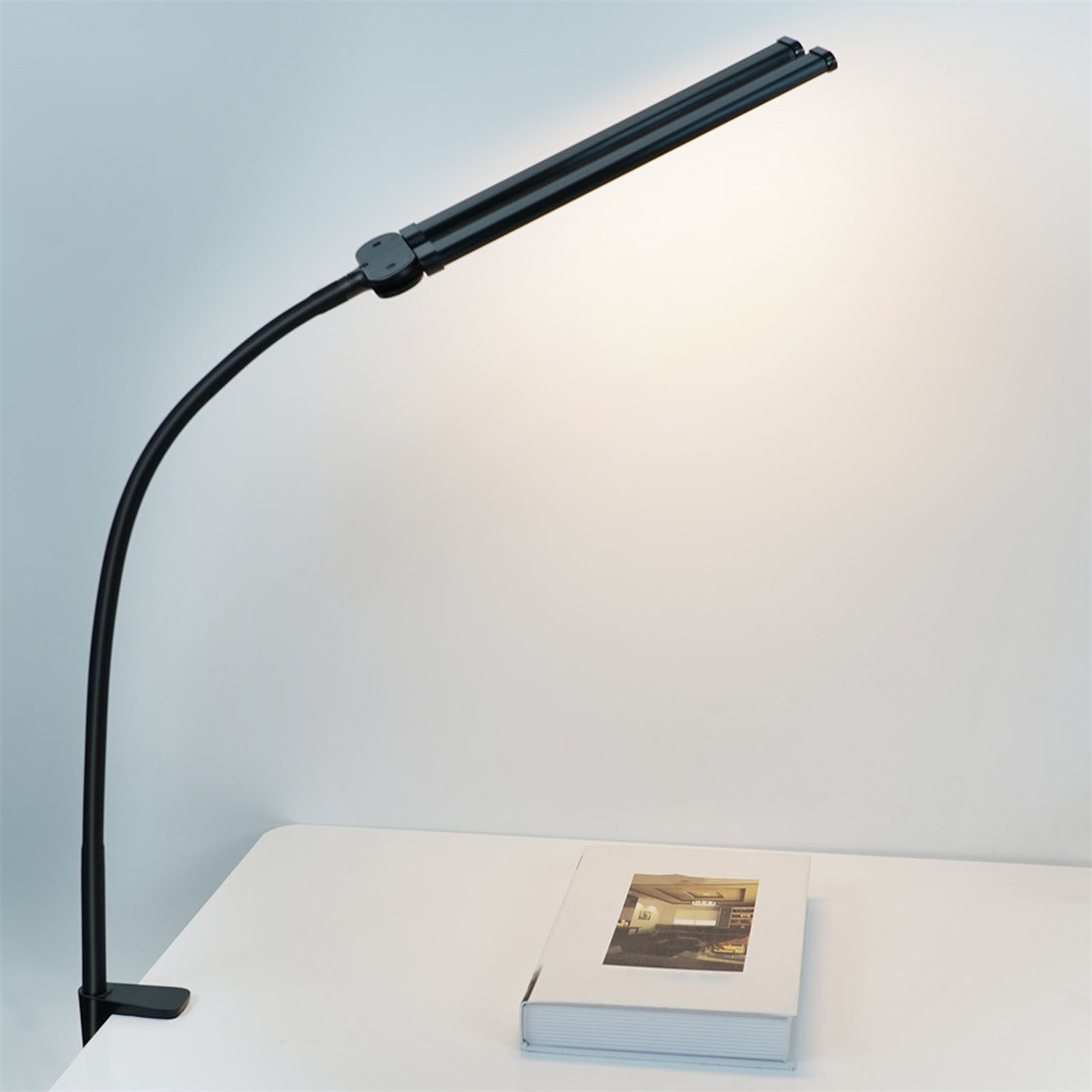 Eine schwarze Schreibtischlampe mit Schwanenhals. Die Lampe ist gebogen und hat zwei LED-Leuchten. Sie steht auf einem weißen Schreibtisch.