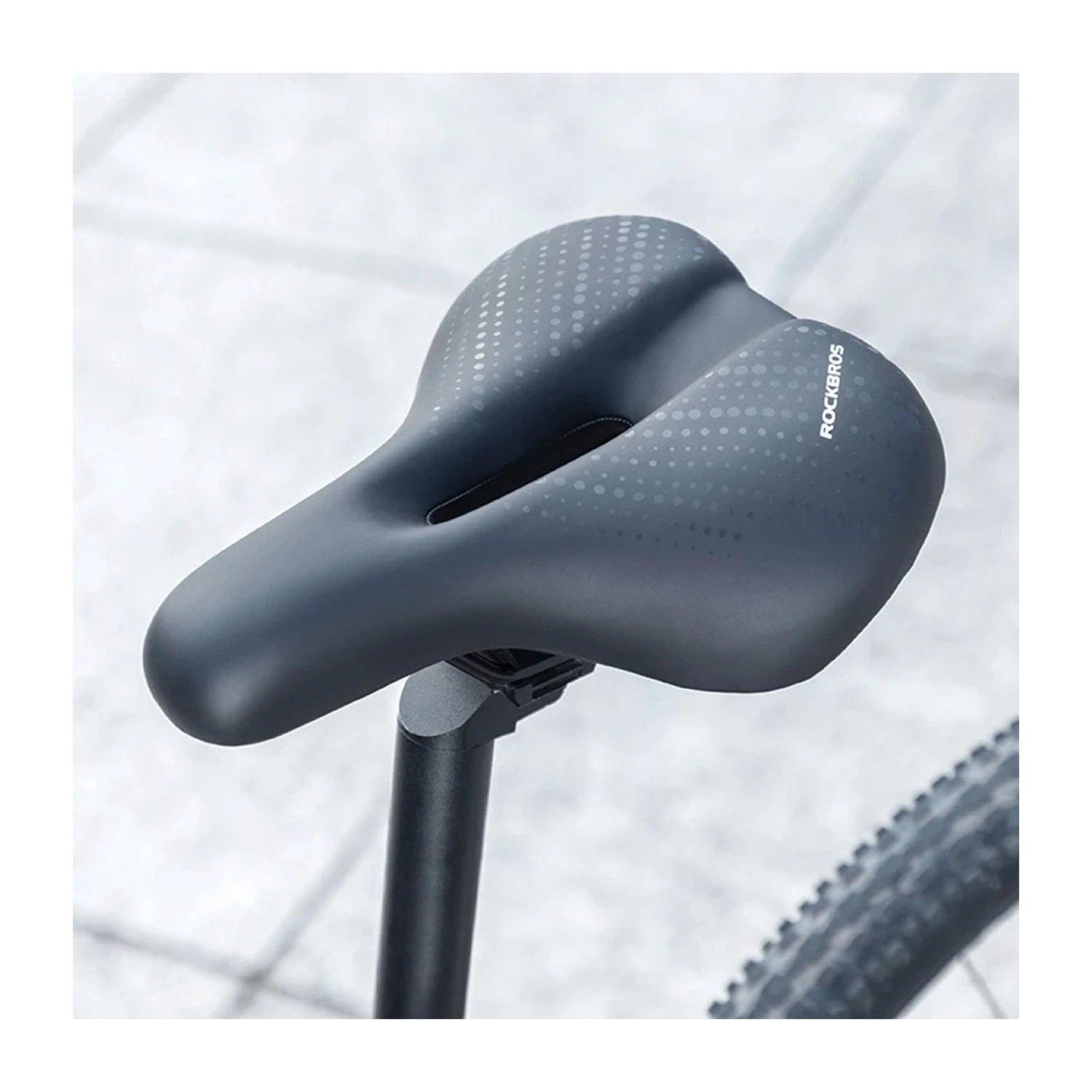 Czarne siodełko rowerowe jest przymocowane do czarnej sztycy podsiodłowej, z szarym tłem.