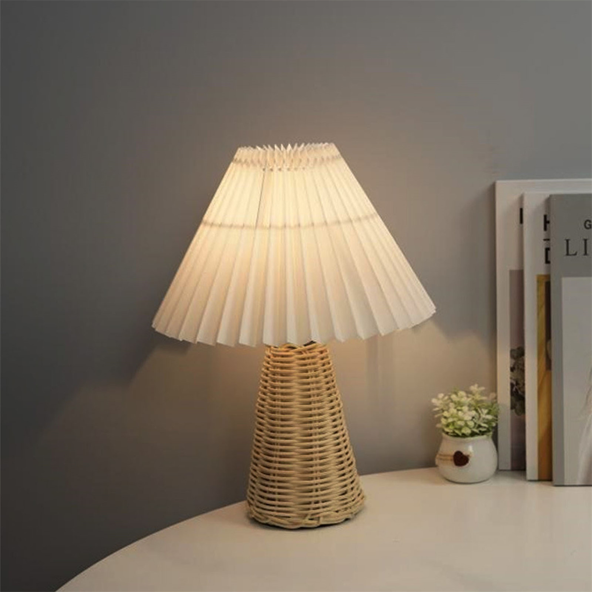 Eine Tischlampe mit einem plissierten weißen Lampenschirm und einem gewebten Rattansockel.
