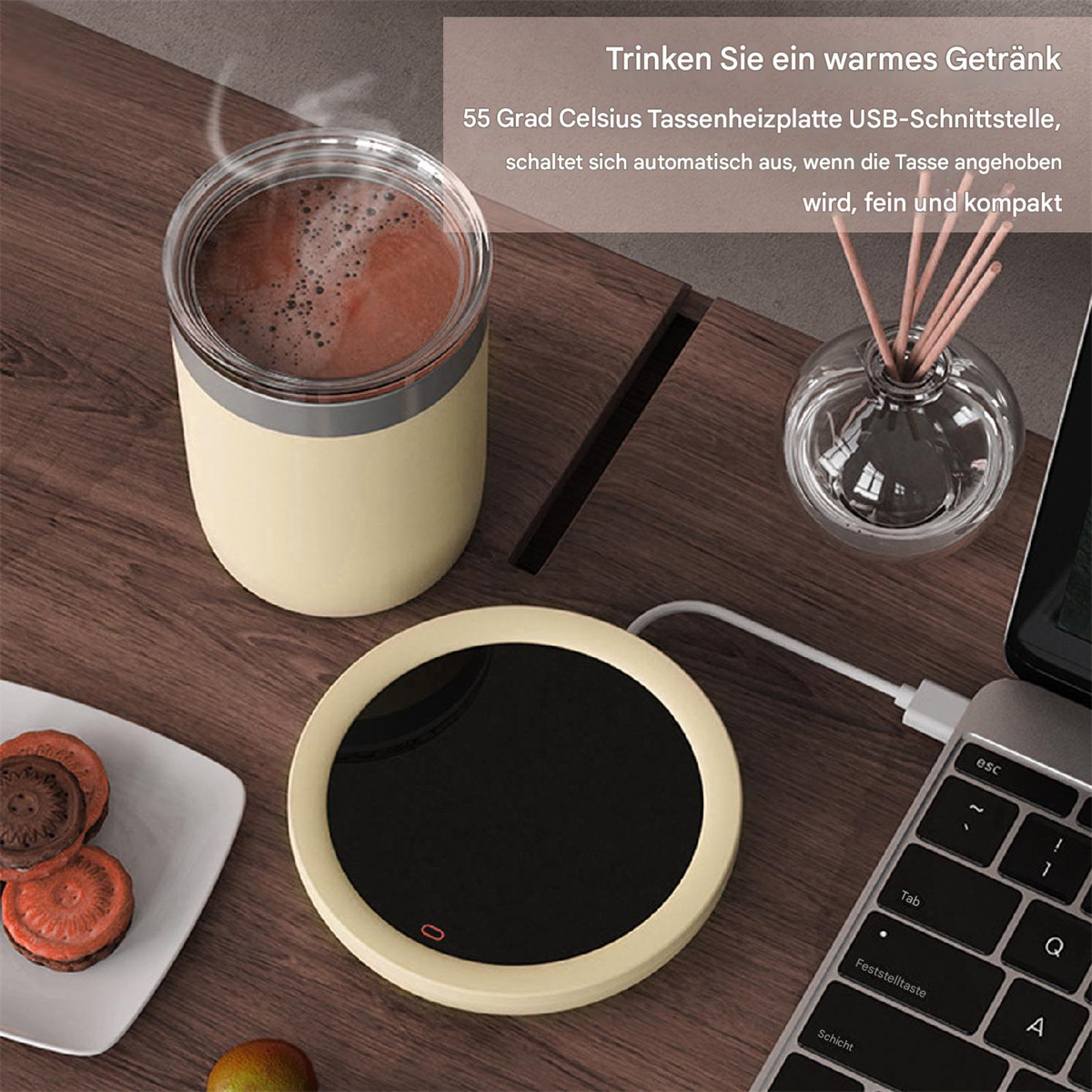 Eine Tasse Kaffee auf einem Wärmer, neben einem Diffusor und einem Laptop. Außerdem Kekse auf einem Teller.