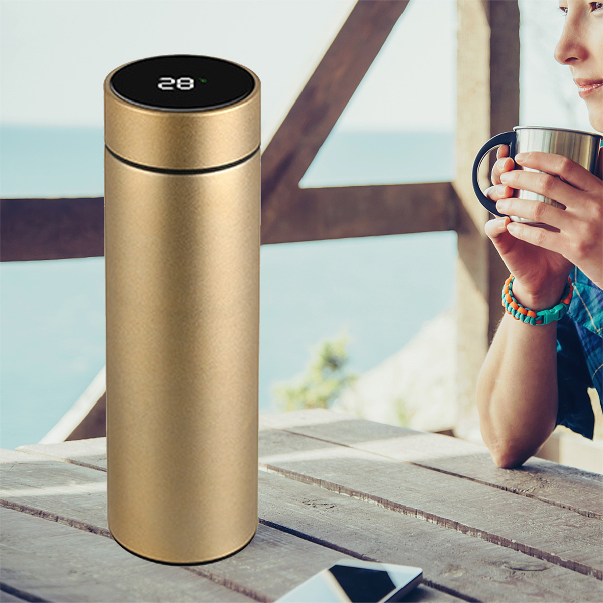 Goldene Thermosflasche mit Digitalanzeige 28. Eine Person hält einen Becher.