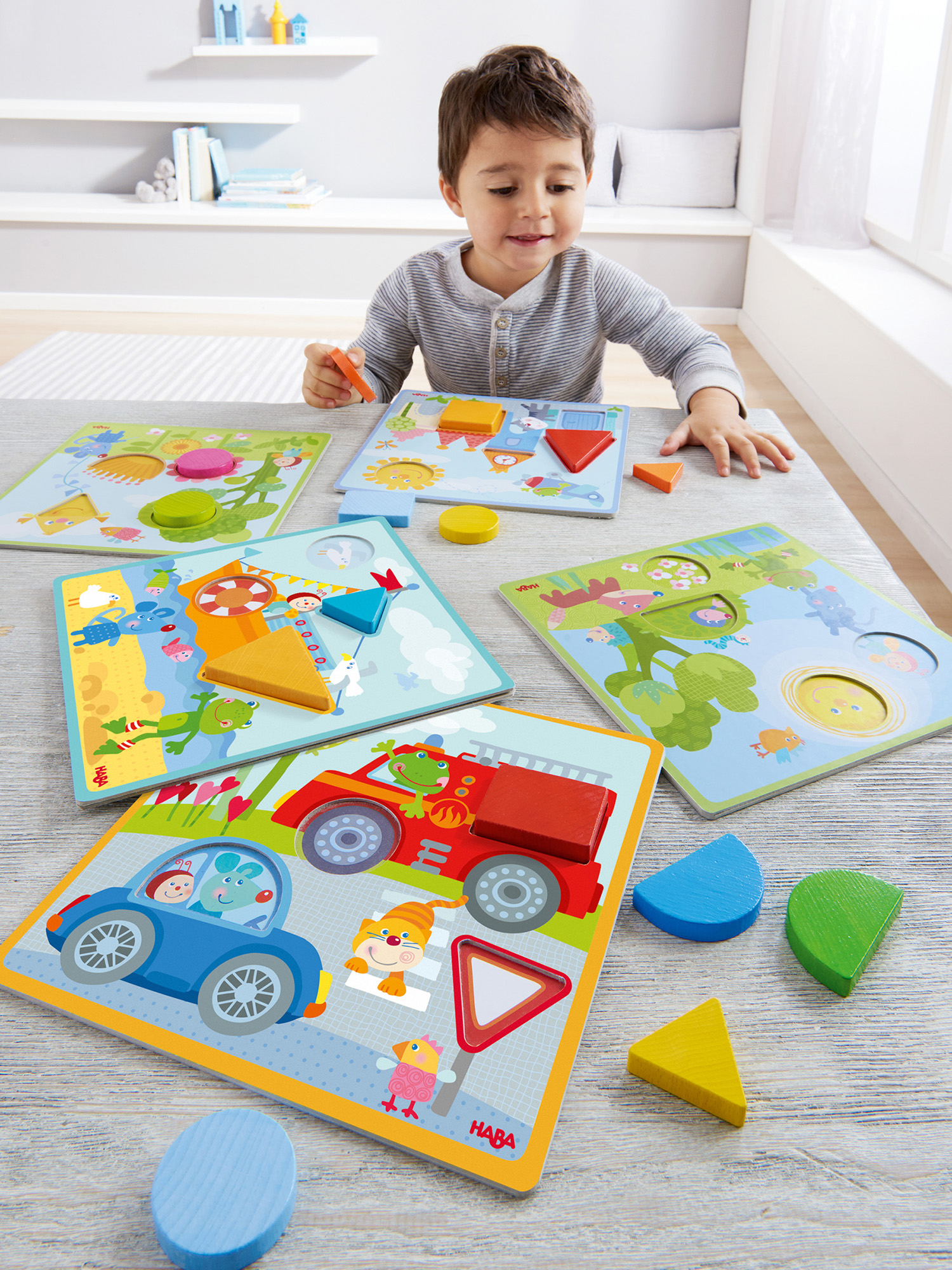 Ein kleiner Junge spielt mit bunten Holzpuzzles auf einem hellen Tisch.