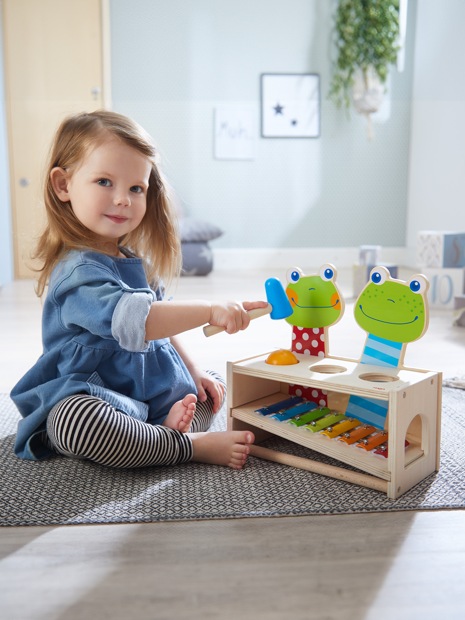 Ein junges Mädchen spielt mit einem Holzspielzeug mit Froschgesichtern und einem Xylophon.