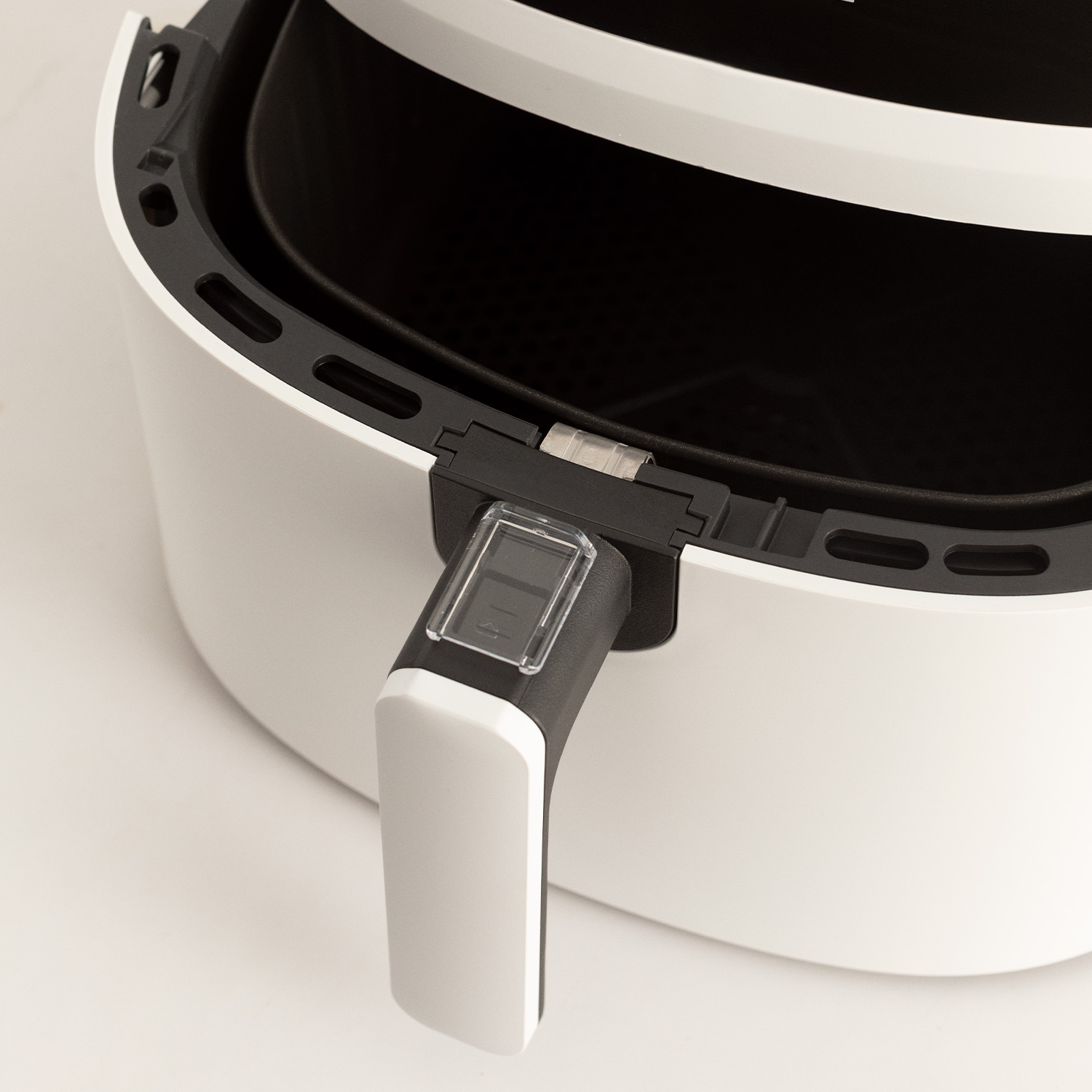 Biała frytkownica powietrzna z czarnym uchwytem i widoczną komorą. Uchwyt jest przezroczysty.