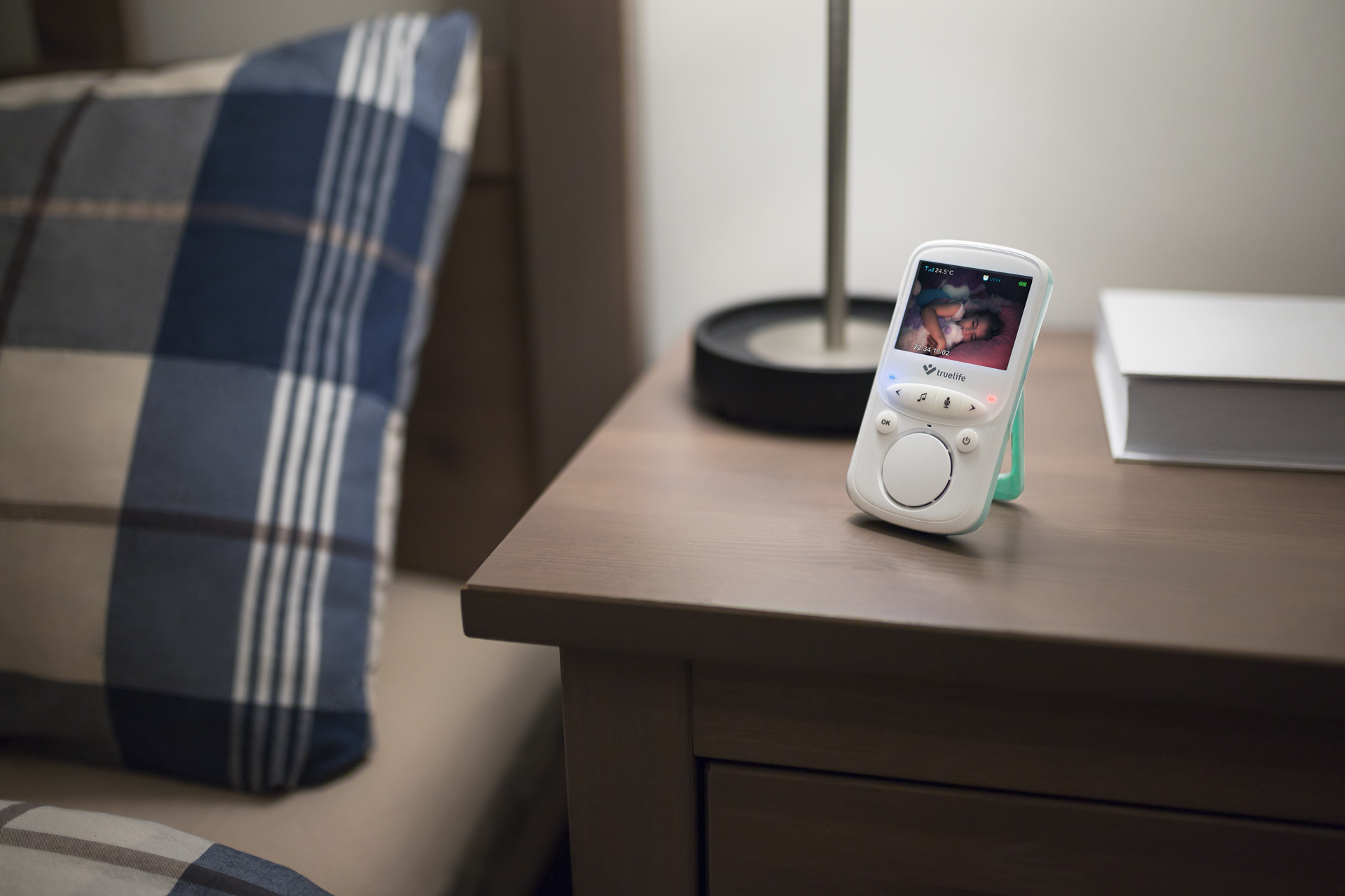 Ein Babyphone auf einem Nachttisch zeigt ein Baby. Ein Kissen und eine Lampe sind im Hintergrund.