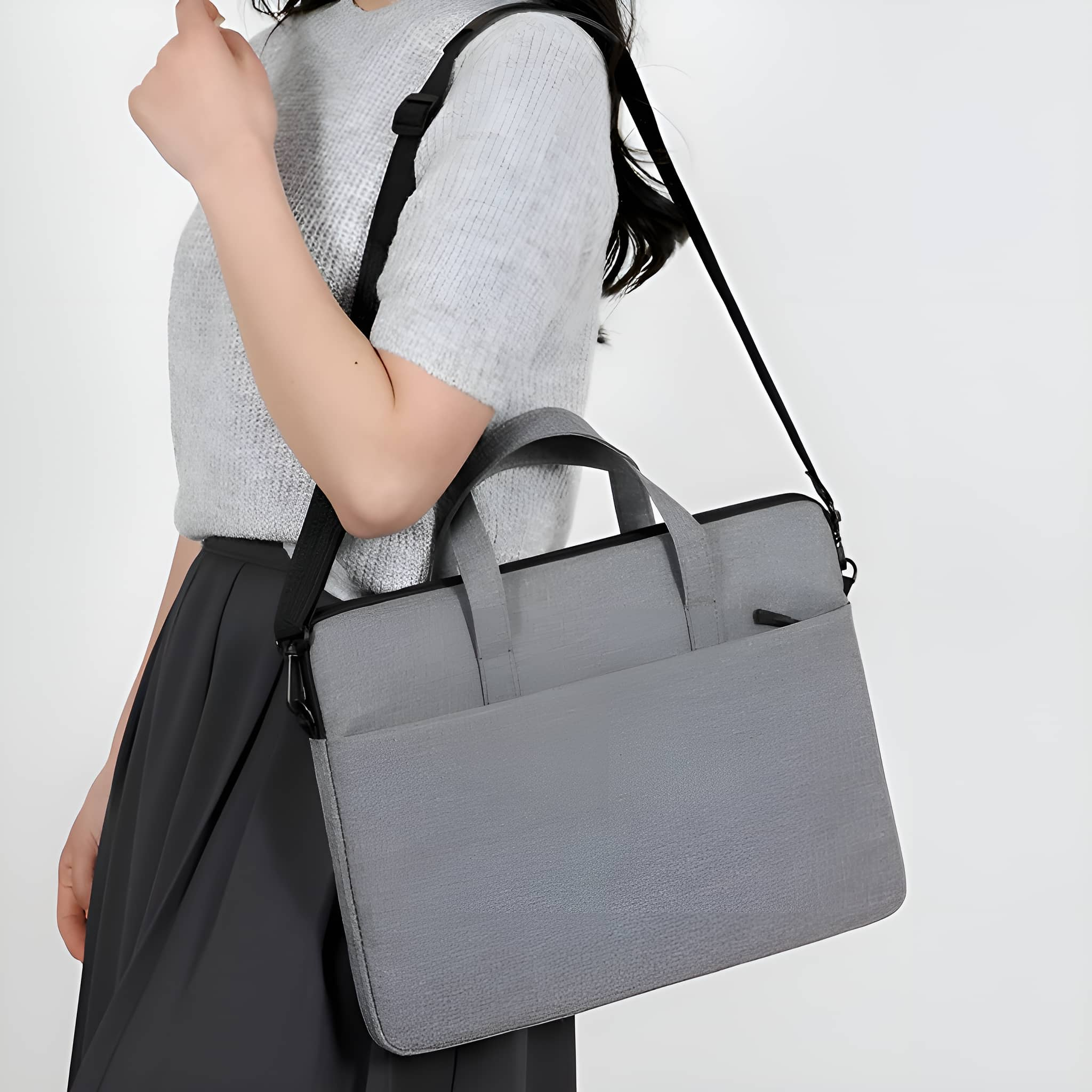 Person trägt eine graue Laptoptasche mit schwarzem Schultergurt. Die Tasche hat einen Griff und eine Tasche.