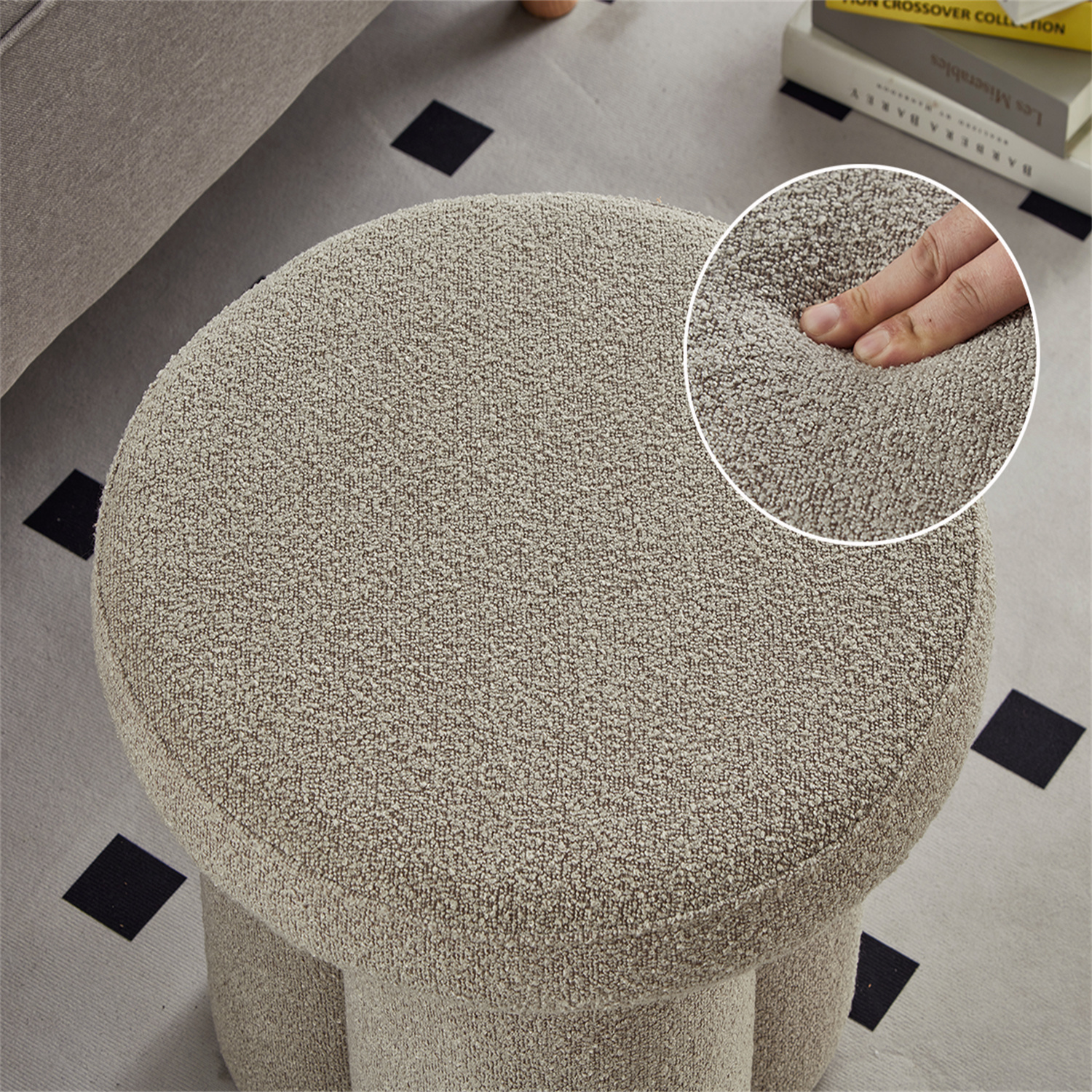 Ein runder, beiger Hocker mit strukturierter Oberfläche. Eine Hand drückt in das Kissen.