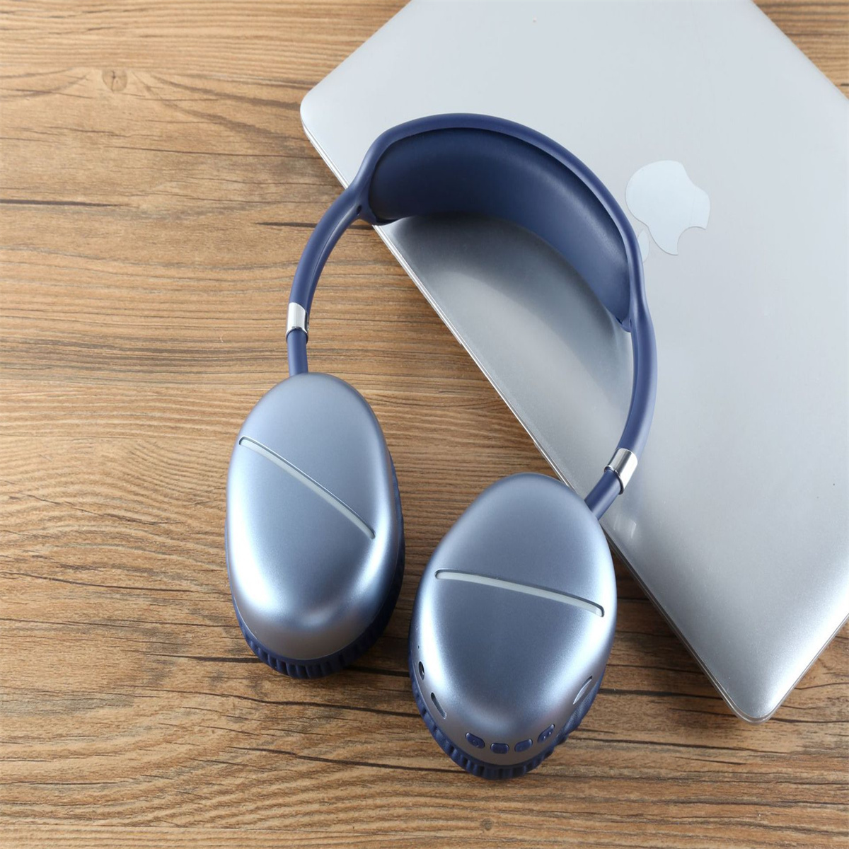 Blaue Kopfhörer auf einem Holztisch, neben einem silbernen Laptop mit Apple-Logo.
