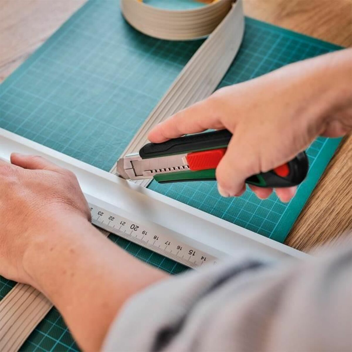 Hände schneiden braunes Material mit einem Cuttermesser auf einer Schneidematte.