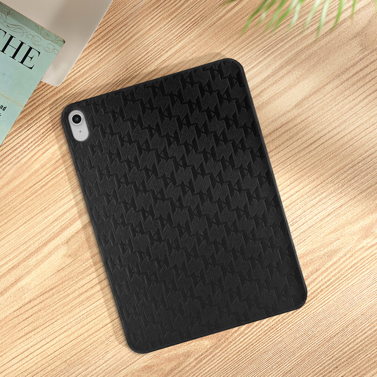 Funda negra para iPad con un patrón repetitivo, colocada sobre una mesa de madera con un libro.