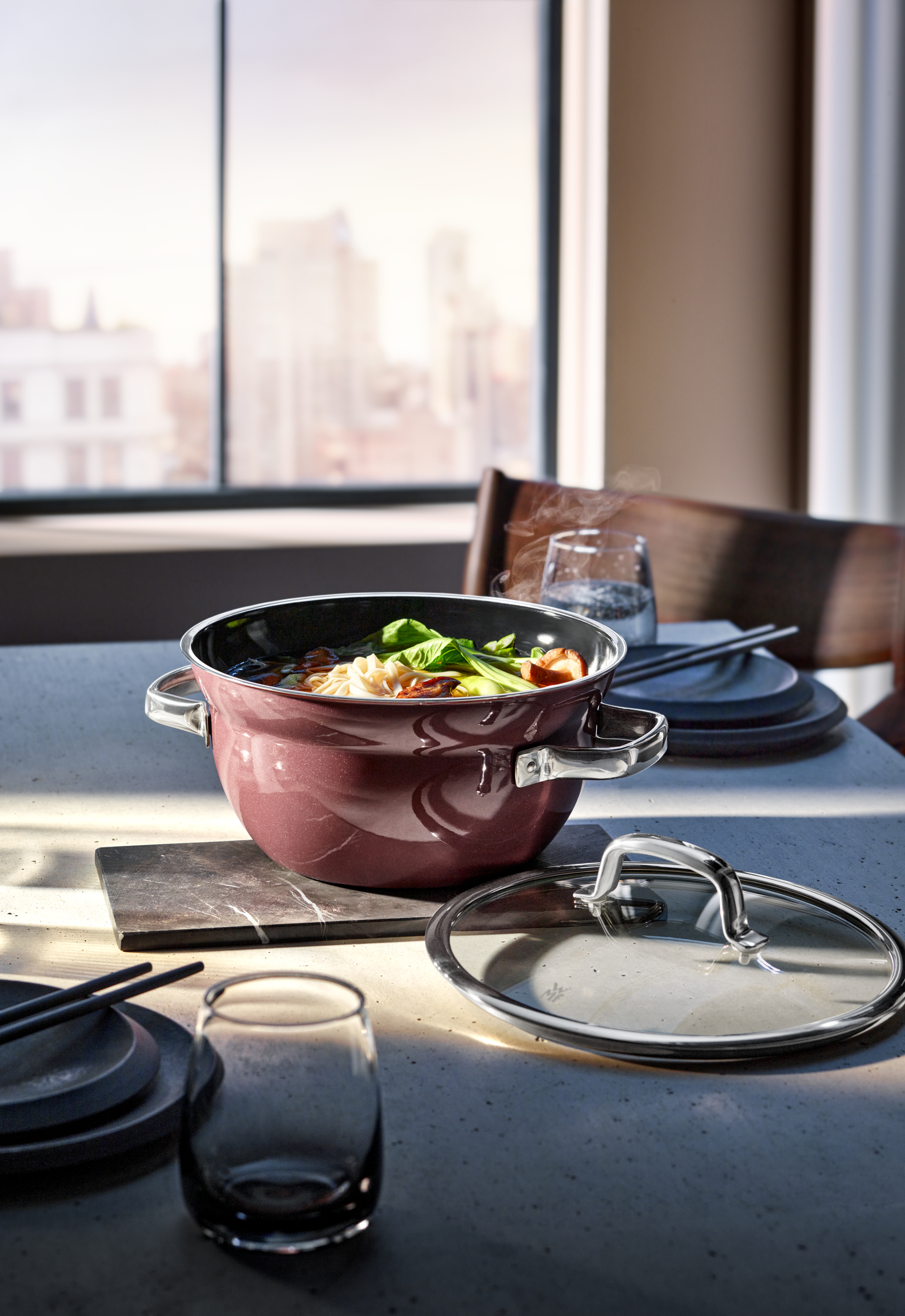 Ein Topf mit Essen auf einem Tisch. Im Hintergrund ein Fenster, Teller und Gläser.
