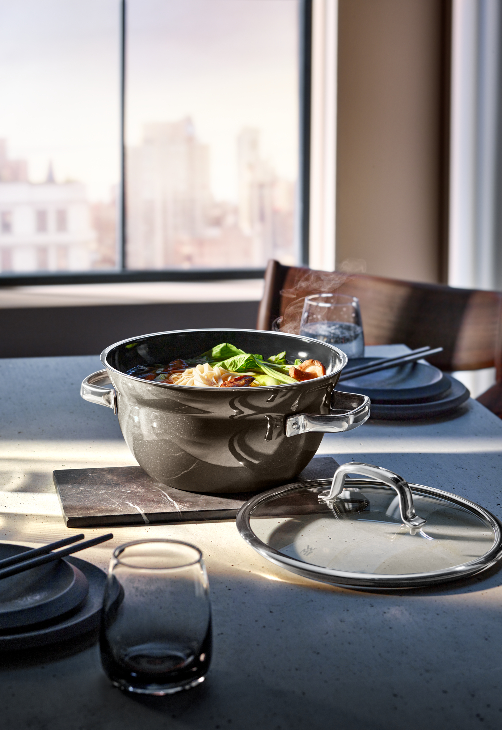 Ein Topf mit Essen auf einem Tisch. Der Topf ist offen, und das Essen ist sichtbar. Ein Fenster ist im Hintergrund.