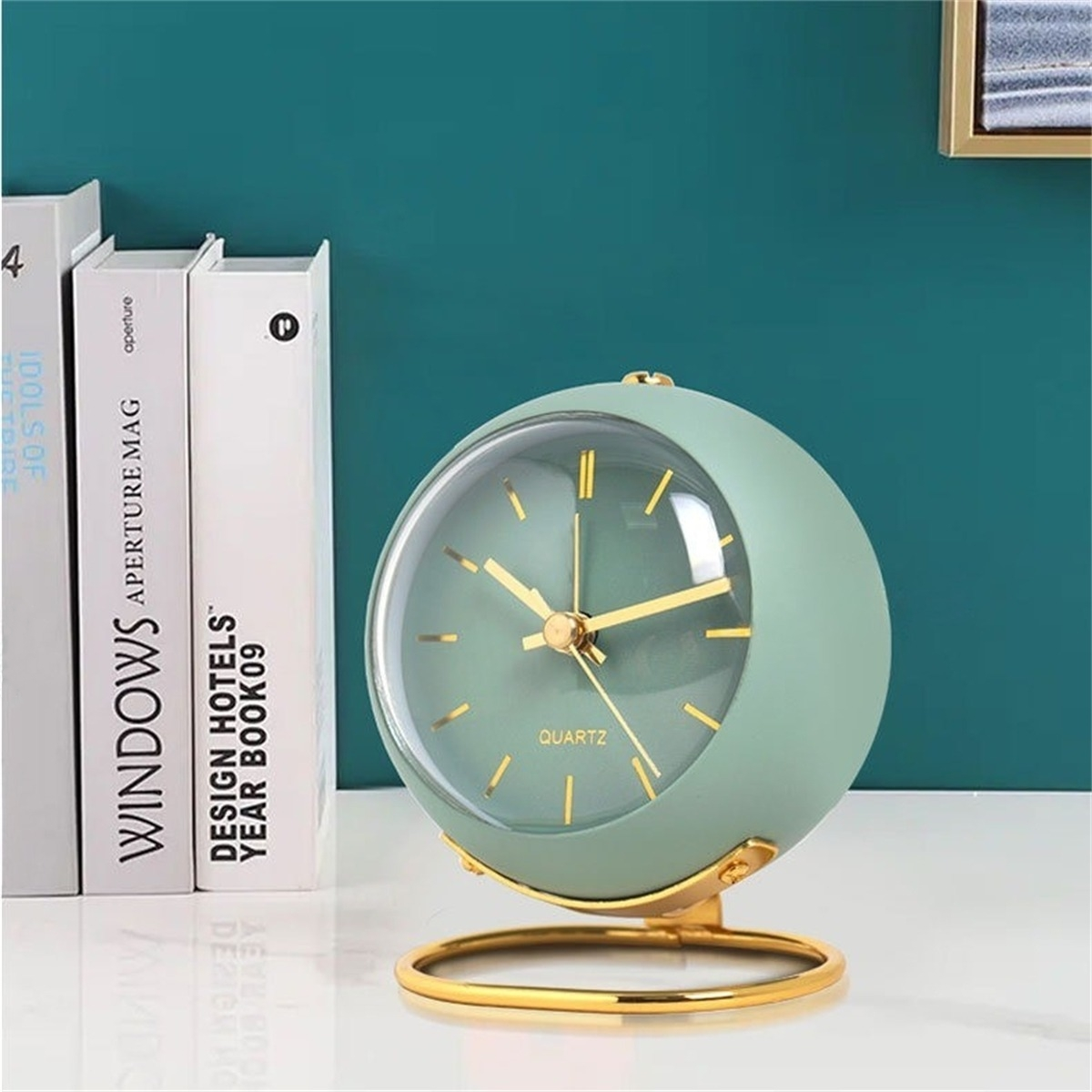 Eine grüne, kugelförmige Uhr mit goldenem Sockel und Zeigern auf weißer Oberfläche.