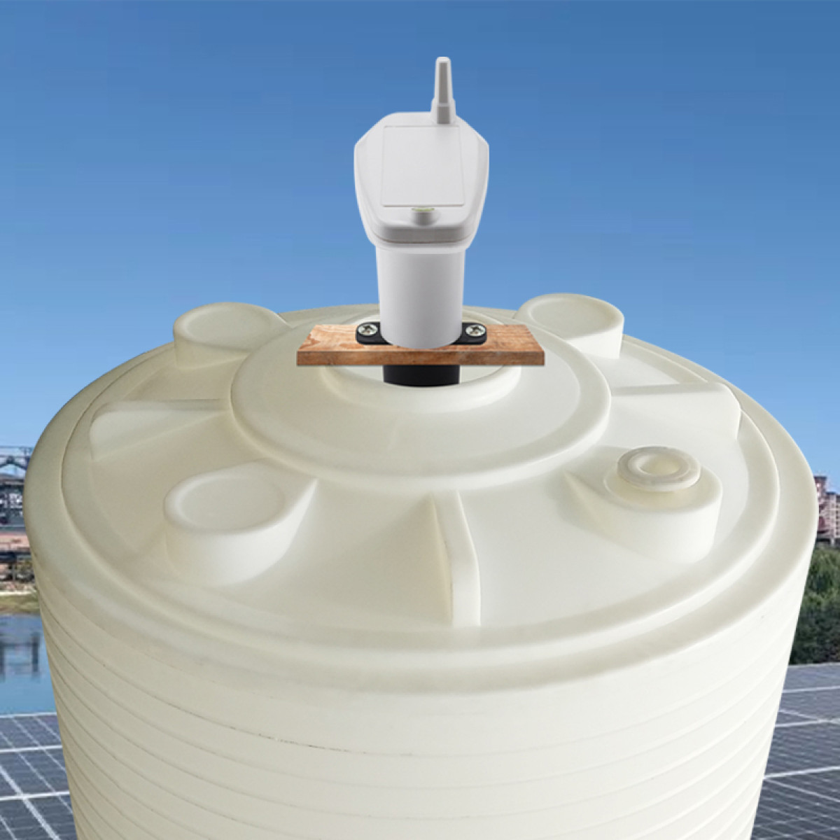 Biały zbiornik z czujnikiem na górze, umieszczony na drewnianej powierzchni, na tle błękitnego nieba.