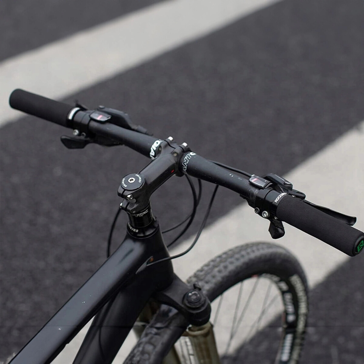 Ein Fahrradlenker mit schwarzen Griffen, Nahaufnahme auf einer Straße.