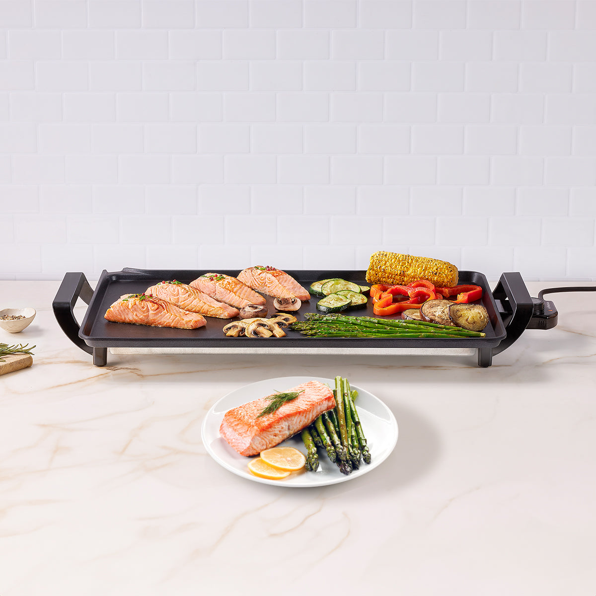 Parrilla eléctrica con salmón cocido, verduras y maíz. Fondo de azulejos blancos y plato con comida.