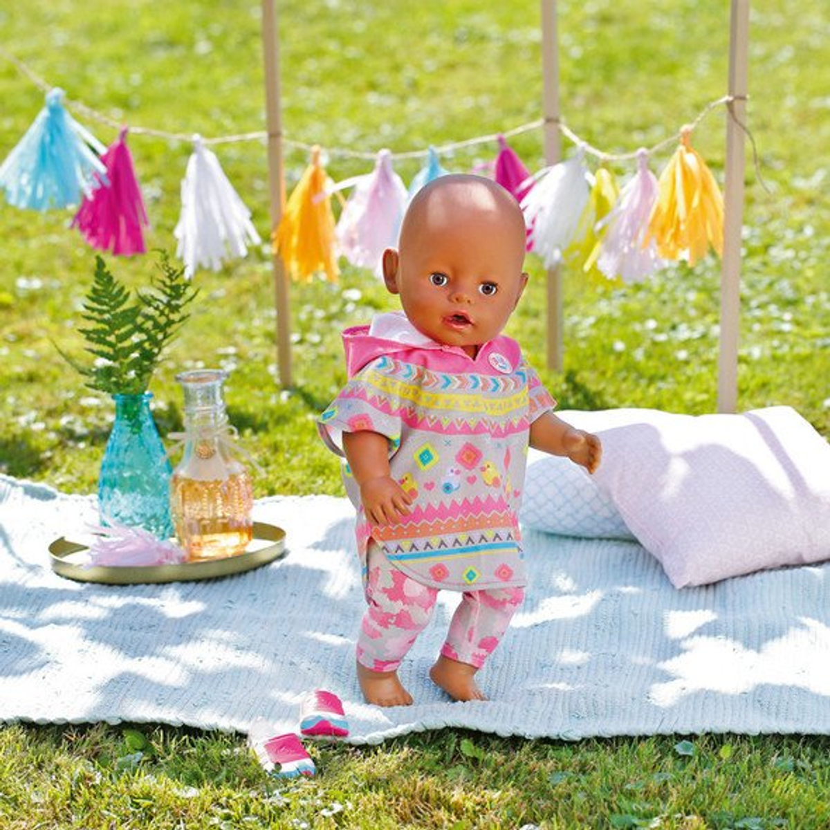 Eine Babypuppe in bunter Kleidung steht draußen mit einem Girlandenhintergrund.