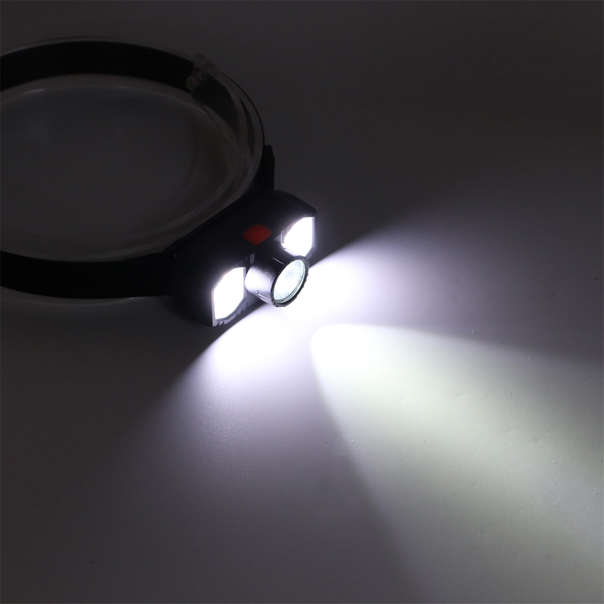 Stirnlampe auf dunkler Oberfläche. Zwei weiße Lichter sind an. Die Stirnlampe ist schwarz mit schwarzem Band.