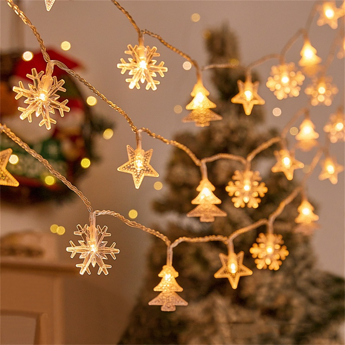 Lichterkette mit Schnee-, Stern- und Baumformen, mit verschwommenem Weihnachtsbaum.