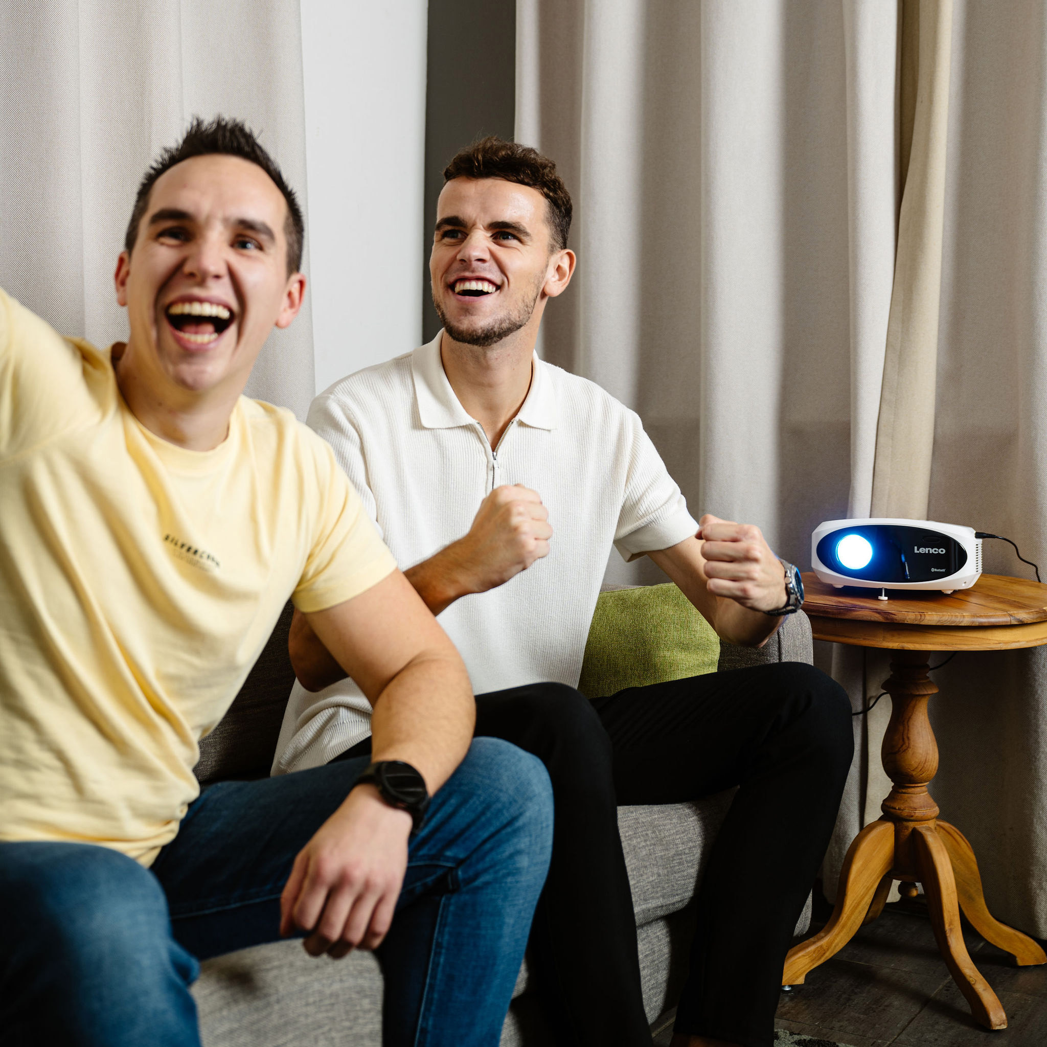 Dwóch mężczyzn ogląda wyświetlany obraz, kibicuje, z projektorem na stole.