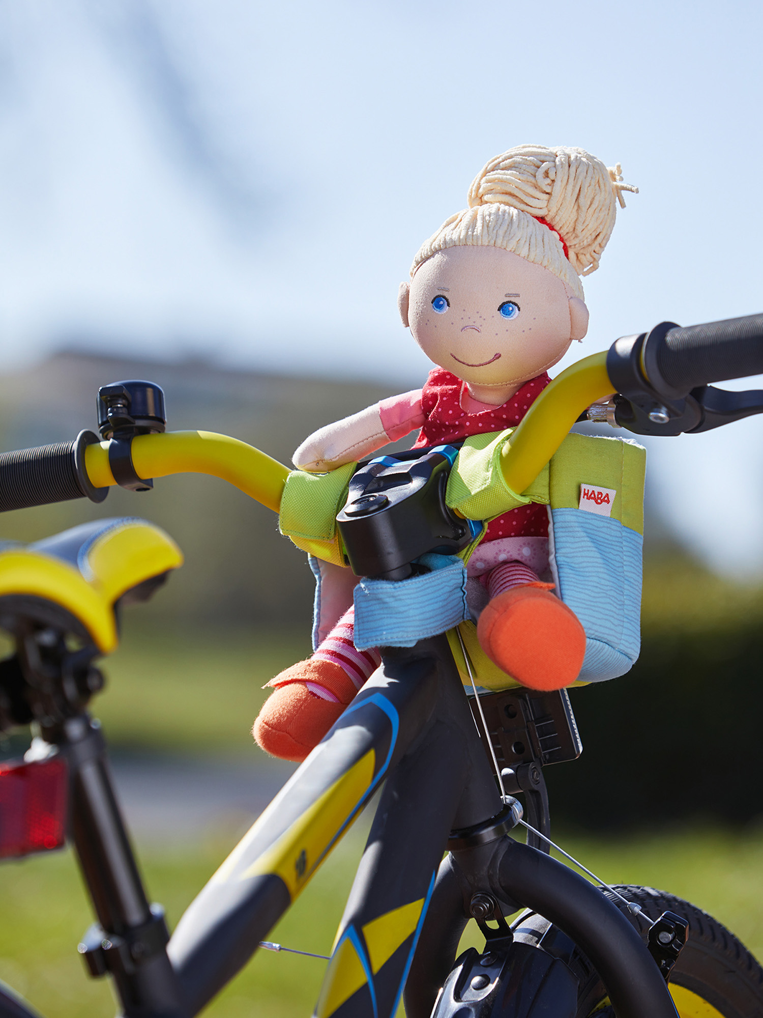 Eine Puppe sitzt auf dem Lenker eines Fahrrads in einem Kindersitz. Sonne im Hintergrund.