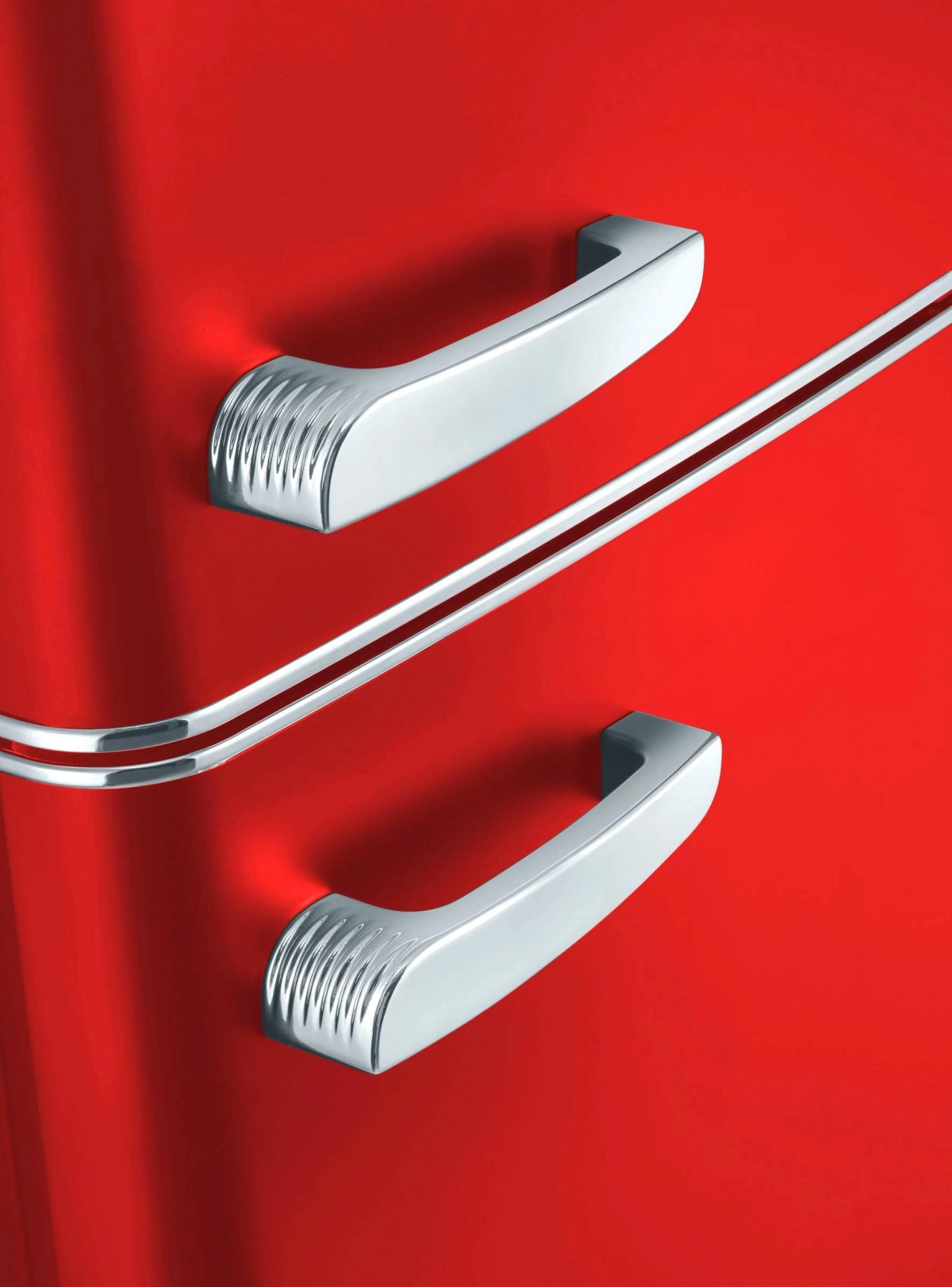 Zbliżenie czerwonych drzwi lodówki z chromowanymi uchwytami i chromowanym paskiem.