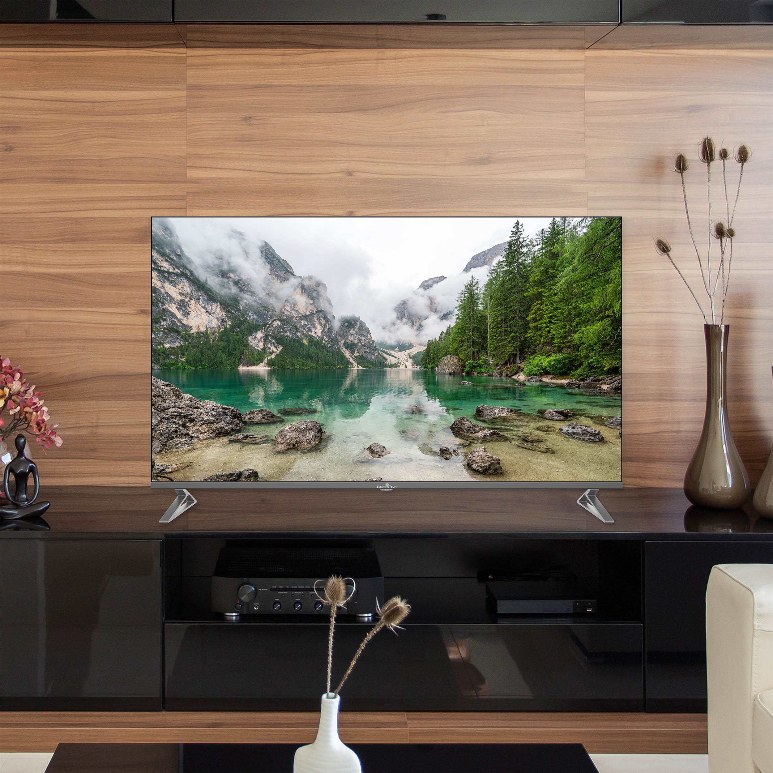 Ekran telewizora wyświetlający malowniczy widok na góry i jezioro. Telewizor stoi na czarnej szafce.