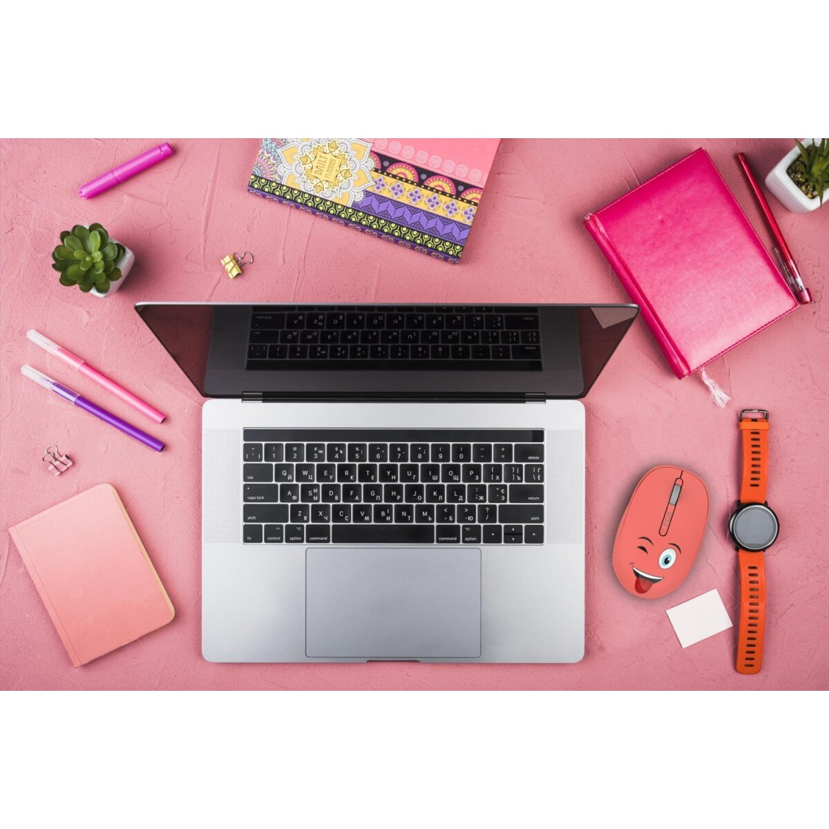 Vista dall'alto di un laptop, mouse, penne, taccuino, orologio e una succulenta. Superficie rosa.