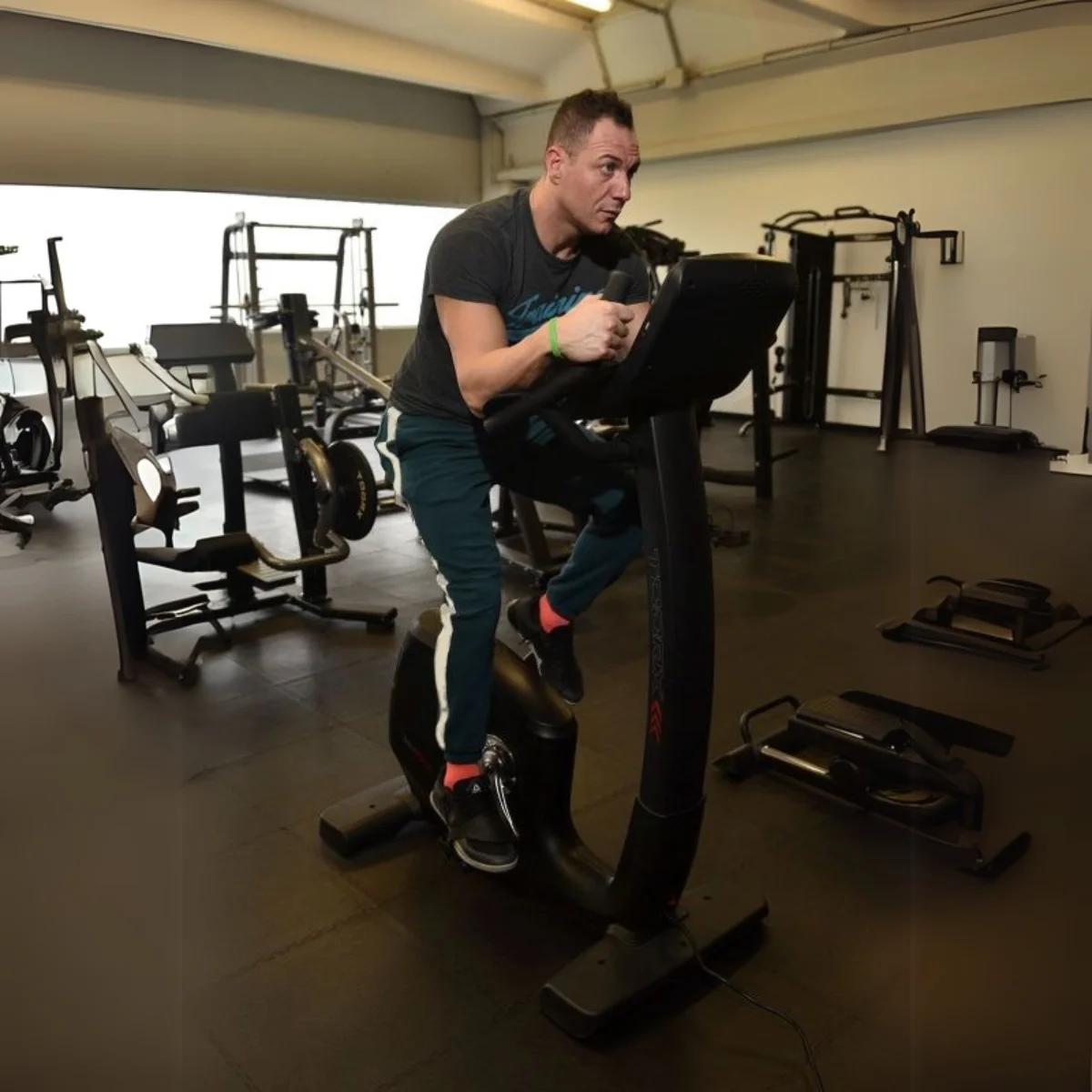 Un homme fait de l'exercice sur un vélo d'appartement dans une salle de sport. La salle de sport est bien éclairée et dispose d'équipements de fitness.