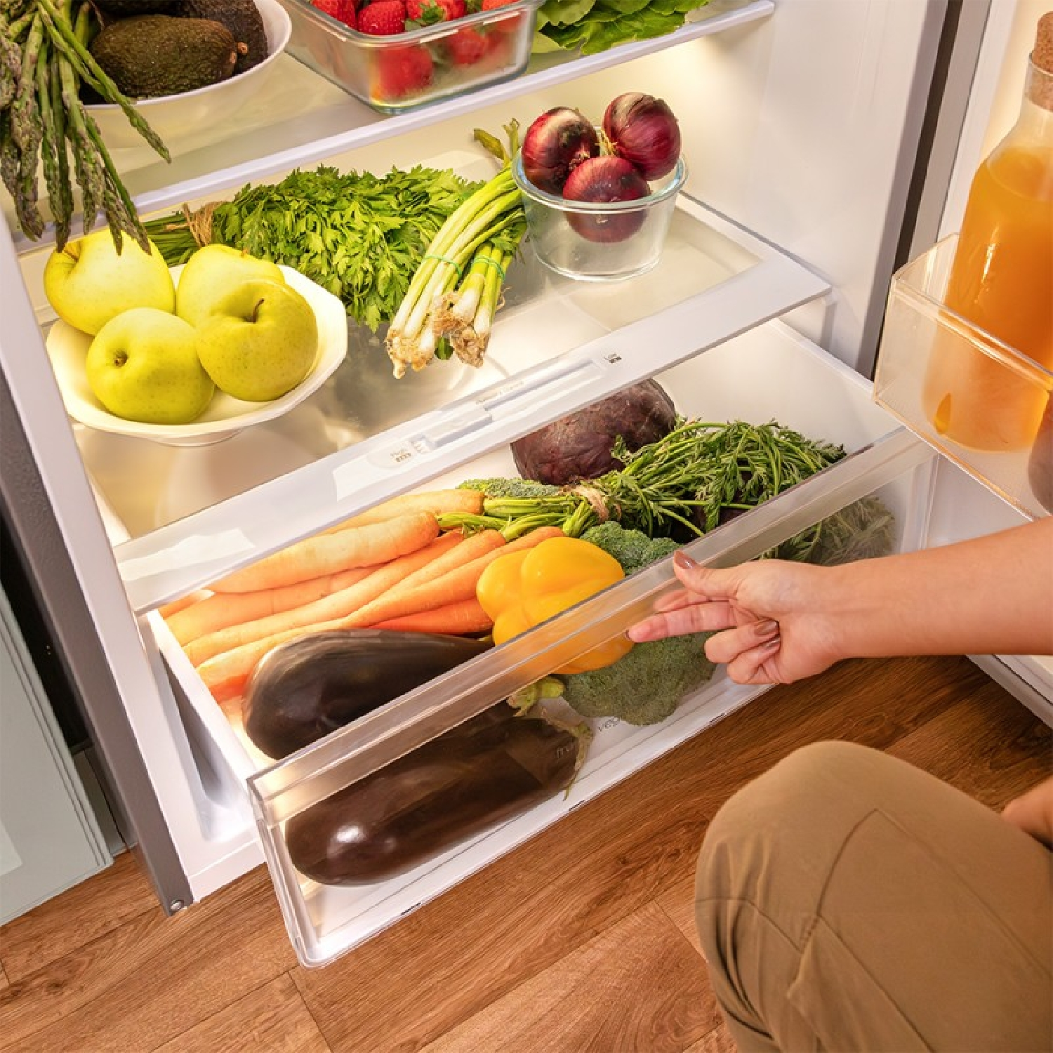 Cajón de refrigerador con verduras; una mano abre el cajón.