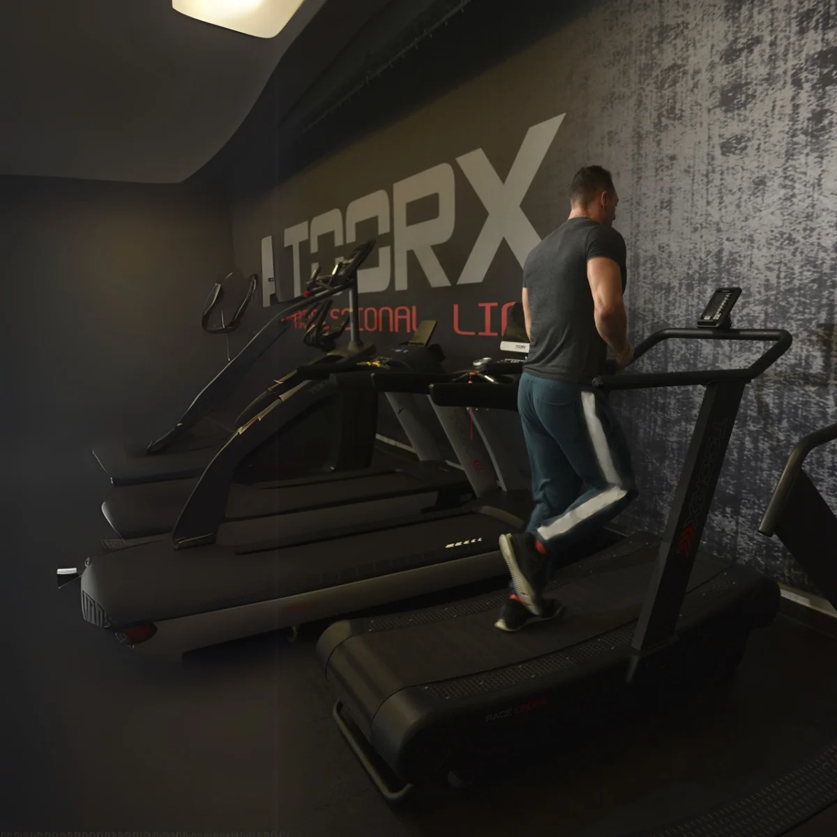 Homme courant sur un tapis roulant dans une salle de sport, autres tapis roulants visibles.