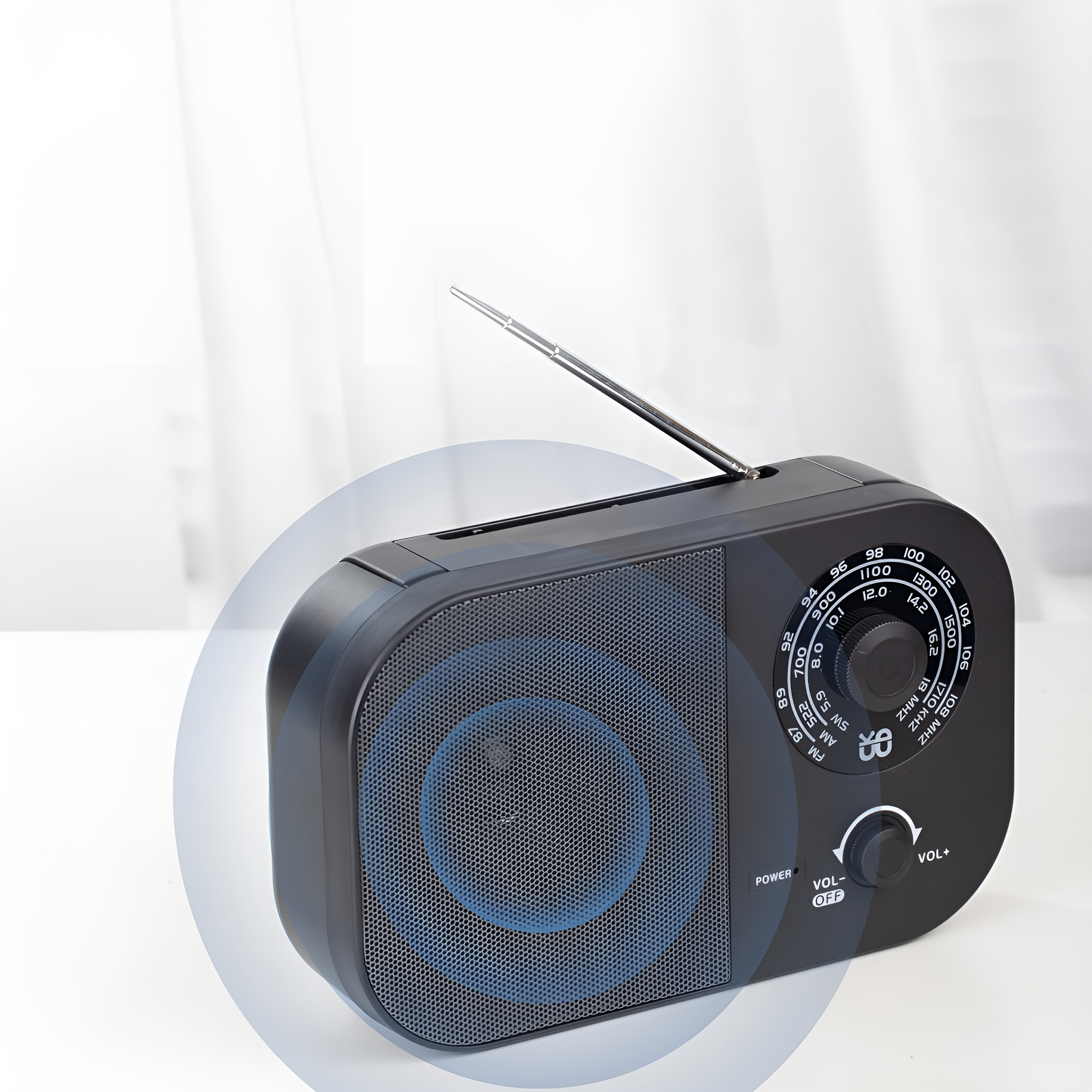 Ein schwarzes Radio mit Antenne, Lautsprecher und Lautstärkereglern vor weißem Vorhanghintergrund.