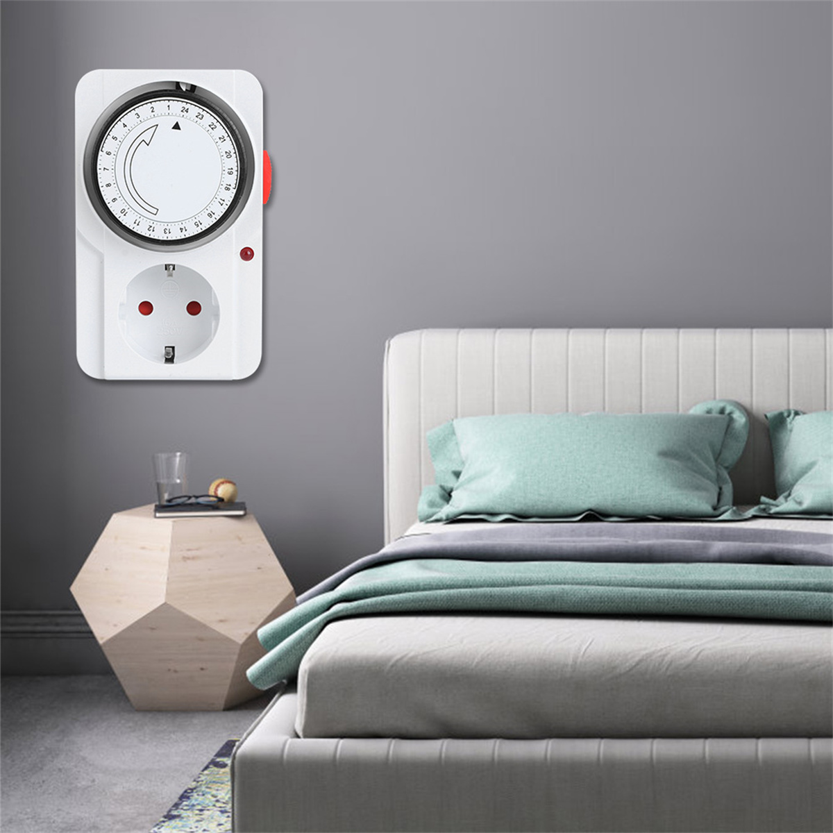 Ein weißer Wandtimer mit roter Taste und Steckdose, platziert neben einem Bett mit grauer Wand.