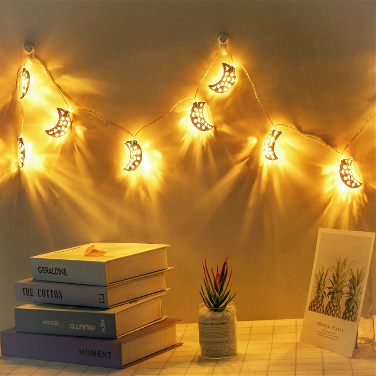 Lichterkette in Mondform an einer Wand mit Büchern, Pflanze und Karte.