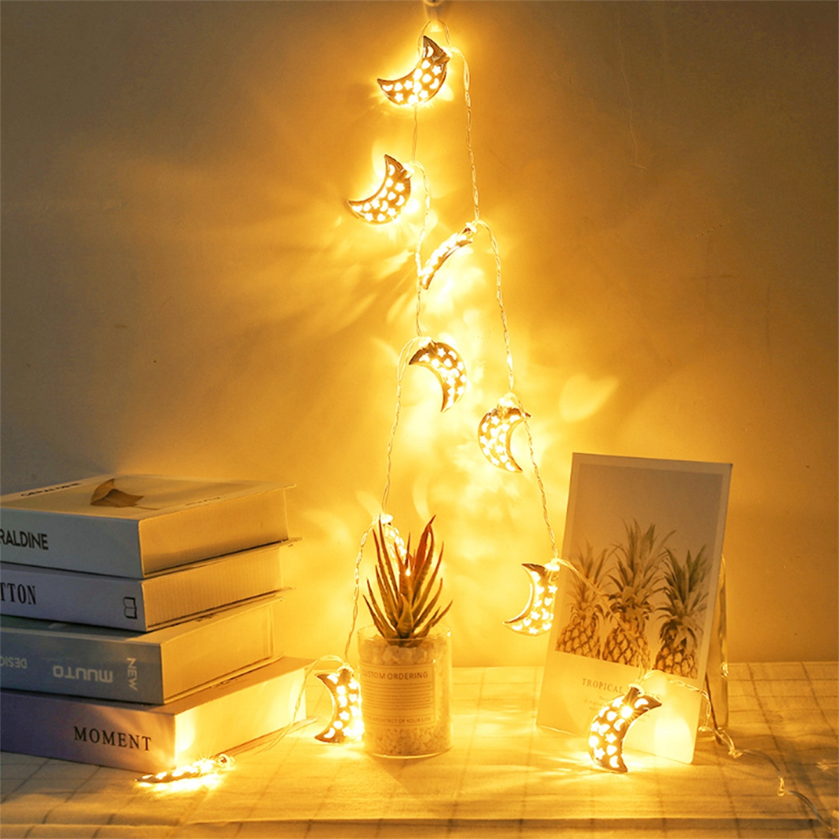Lichterkette mit mondförmigen Lichtern, eine Pflanze, Bücher und ein Bild.