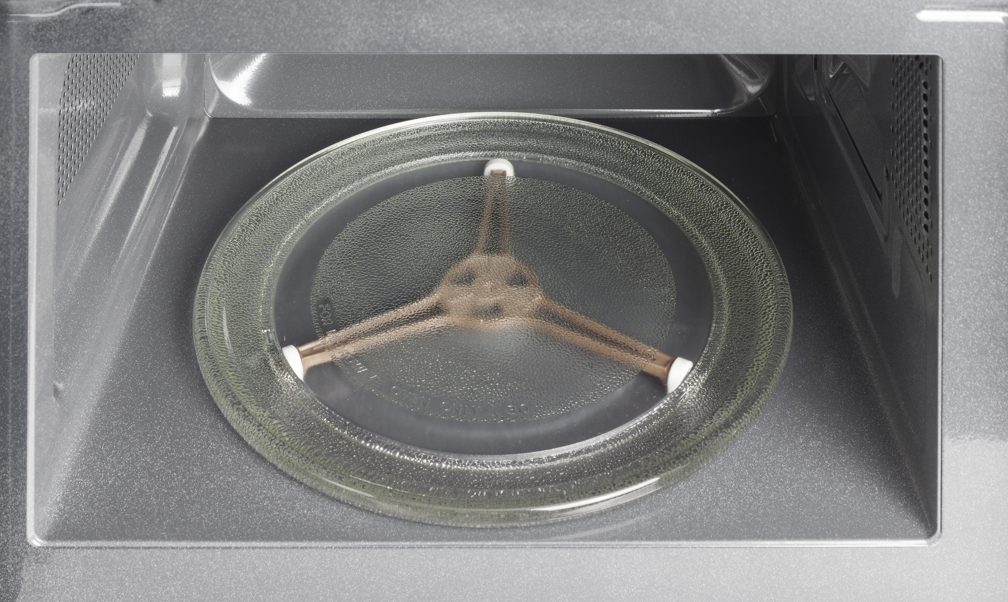L'interno di un forno a microonde, che mostra il piatto rotante in vetro e l'interno. Pareti grigie.