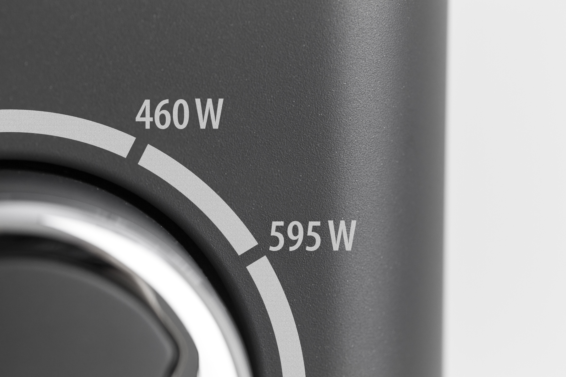 Primo piano di un selettore di potenza grigio scuro che mostra i segni di 460W e 595W su una superficie grigia.