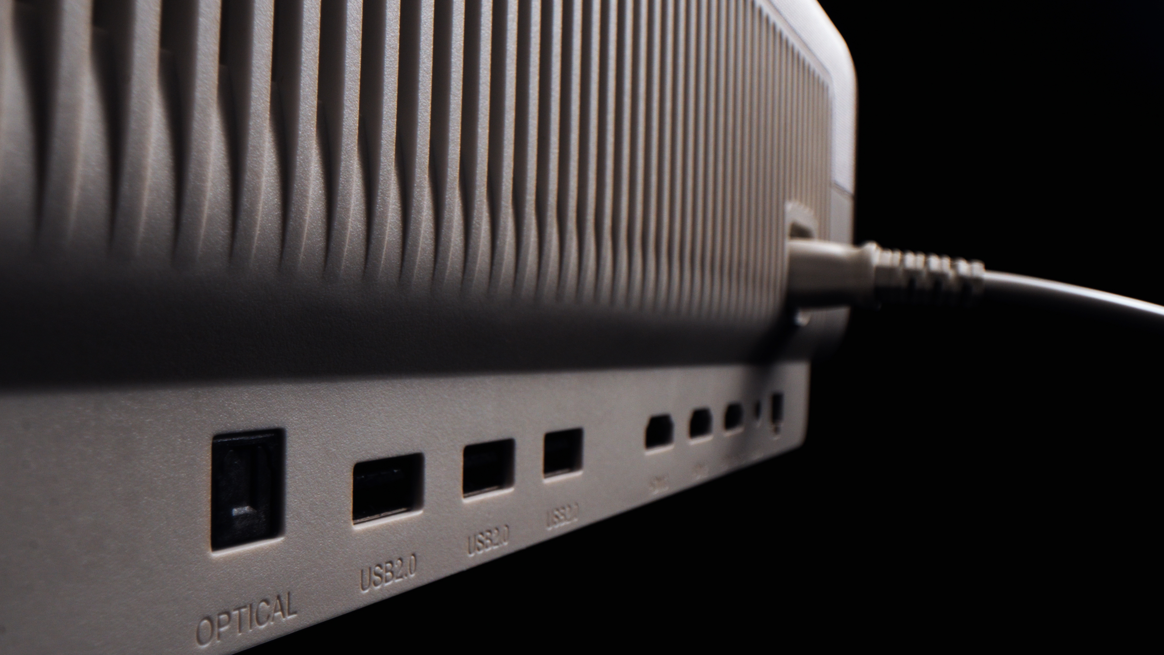 Close-up van een grijze projector met poorten voor optisch, USB en meer, tegen een zwarte achtergrond.
