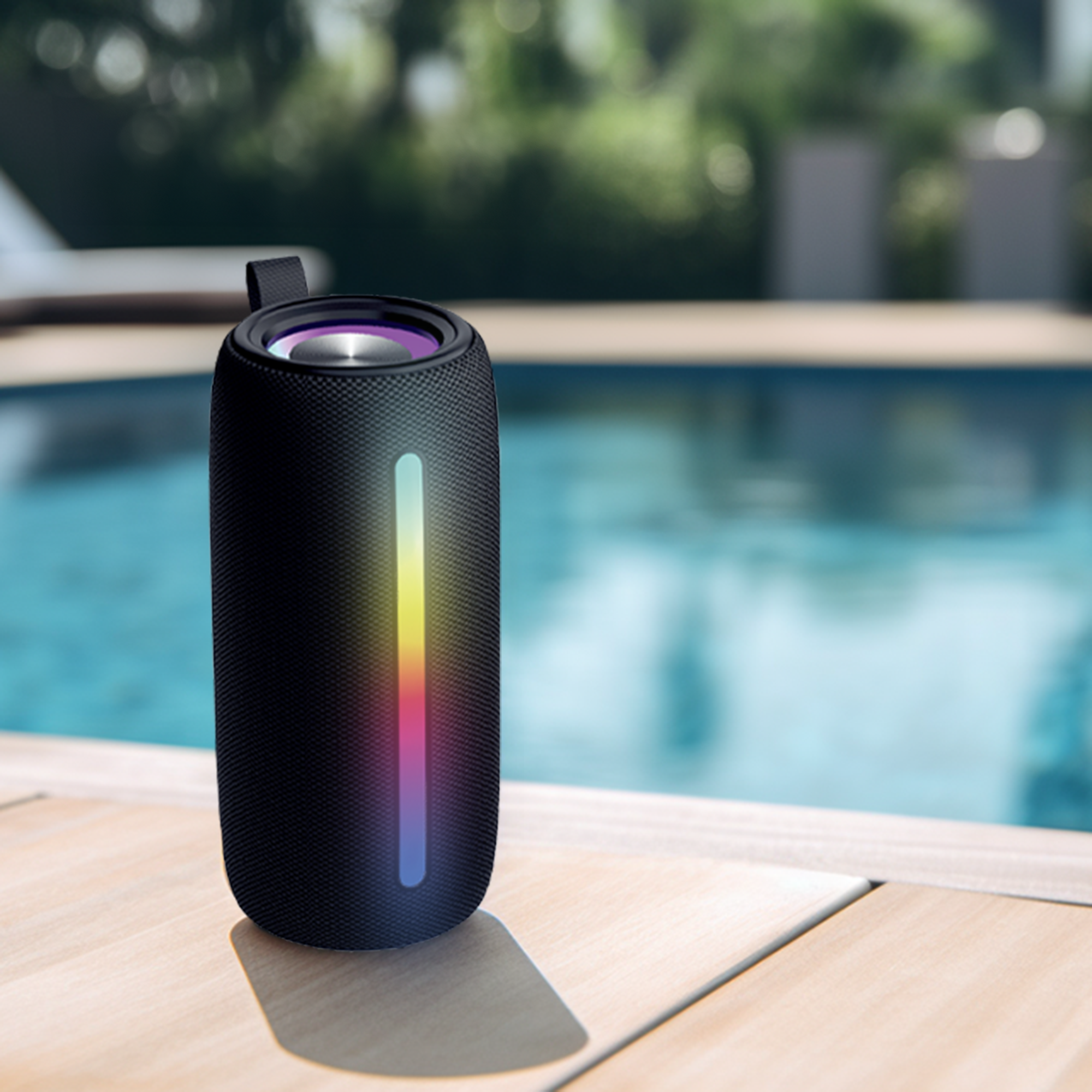 Czarny głośnik z kolorowym paskiem świetlnym, na drewnianym pokładzie. W tle basen.