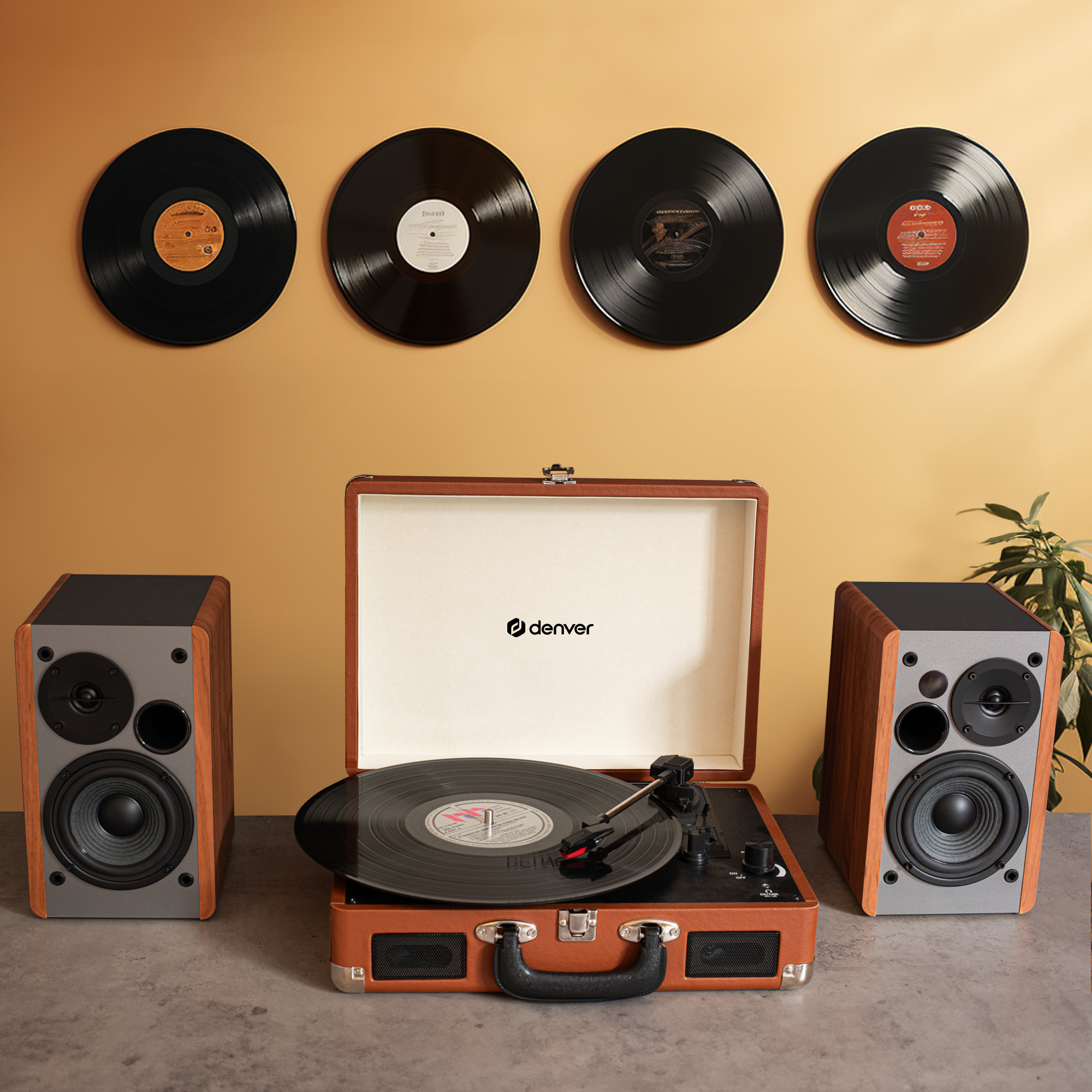 Gramofon z głośnikami i czterema płytami winylowymi wiszącymi na żółtej ścianie.