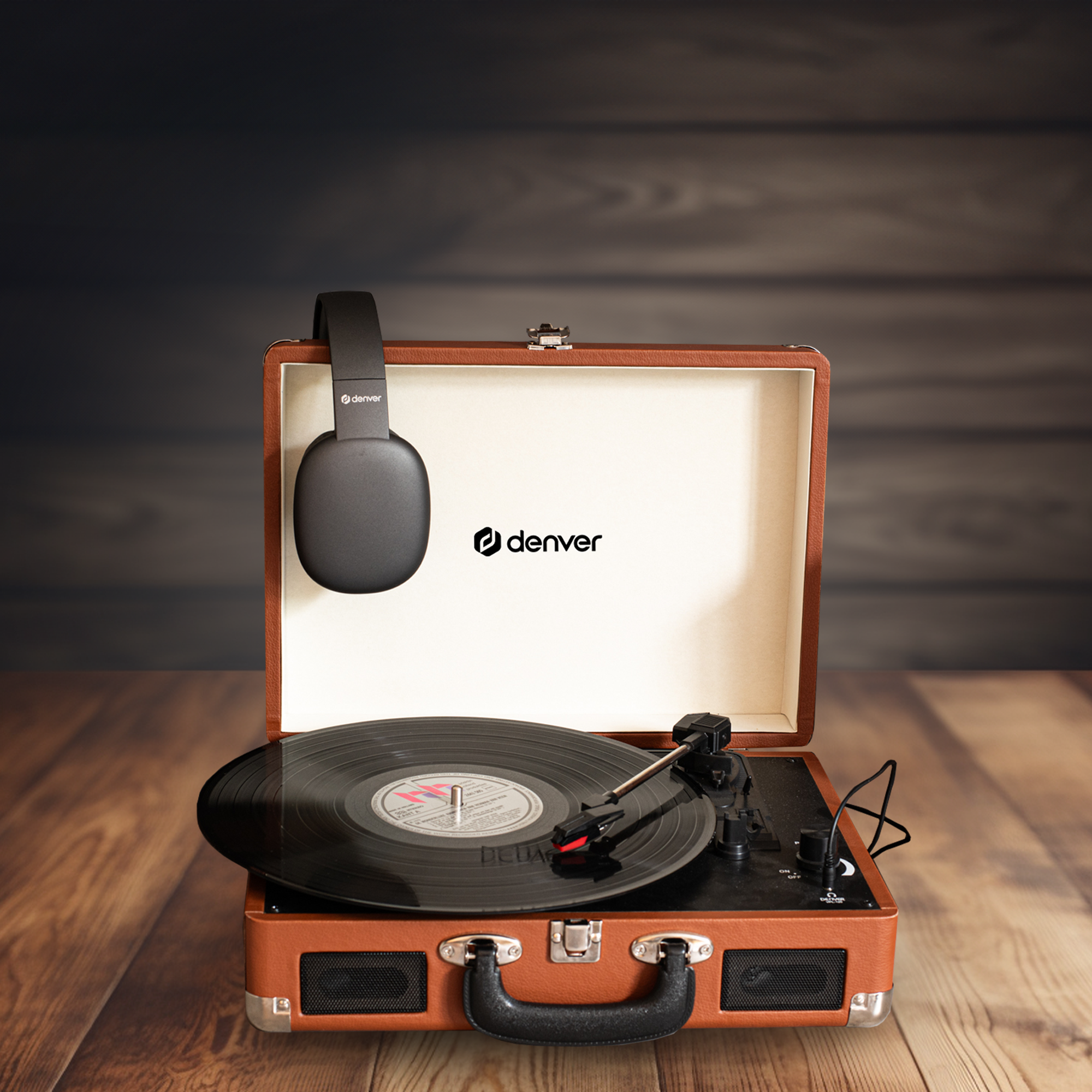 Gramofon w walizkowym etui ze słuchawkami na wierzchu na drewnianej powierzchni.
