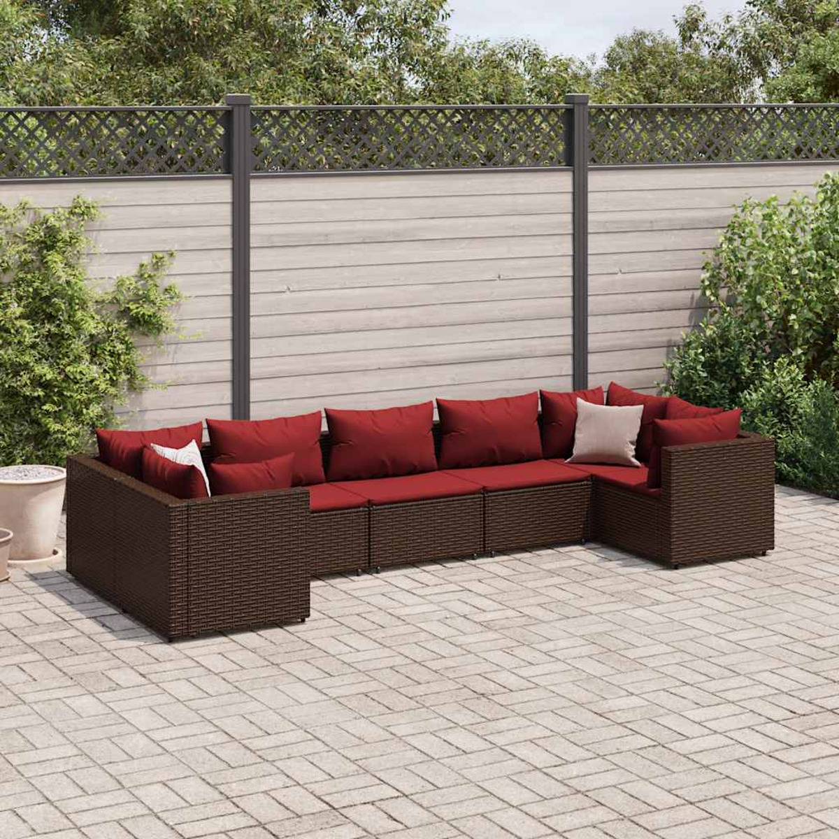 Braunes, gewebtes Outdoor-Ecksofa mit roten Kissen in einem Garten.