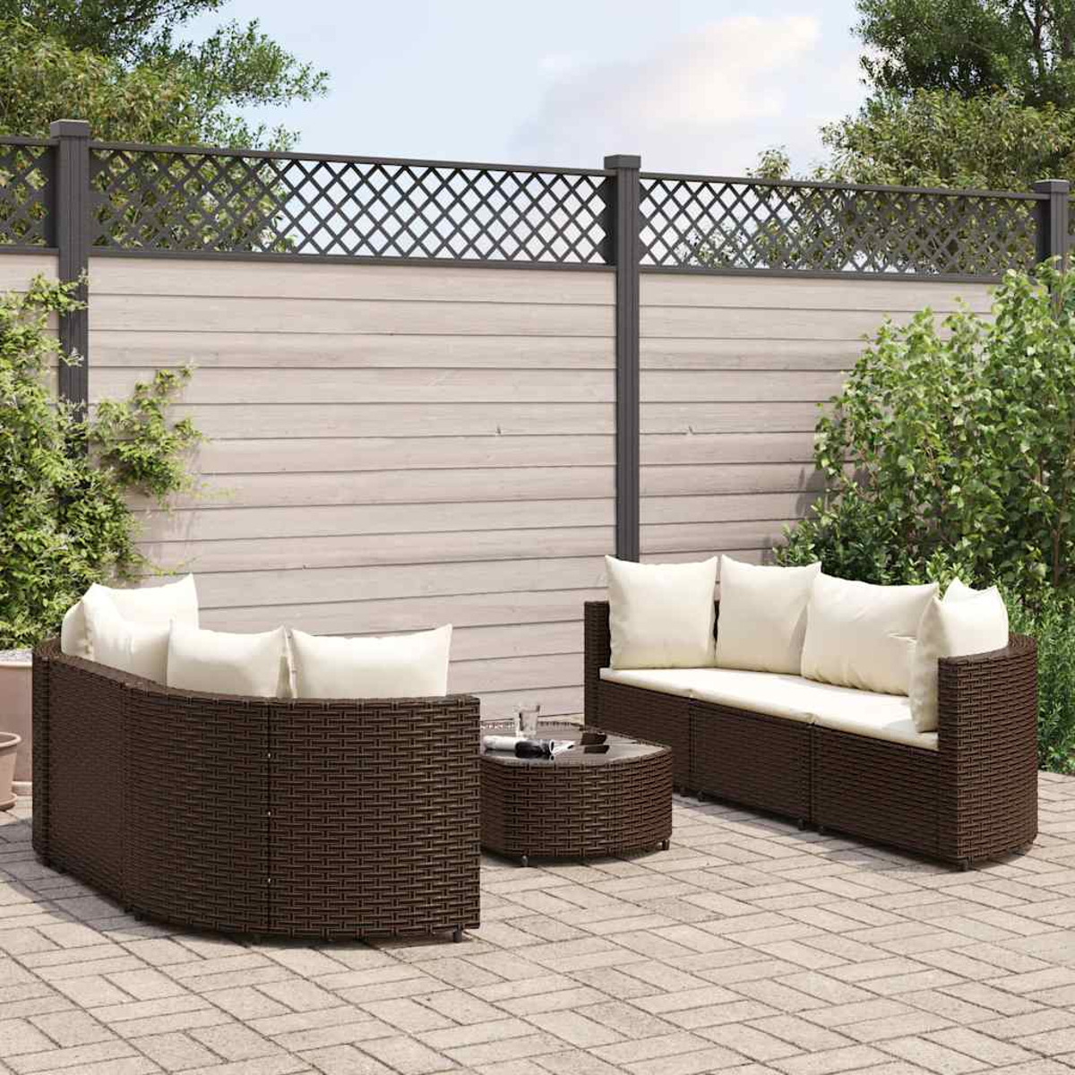 Set patio esterno con mobili in vimini marrone, cuscini e una recinzione a traliccio sullo sfondo.