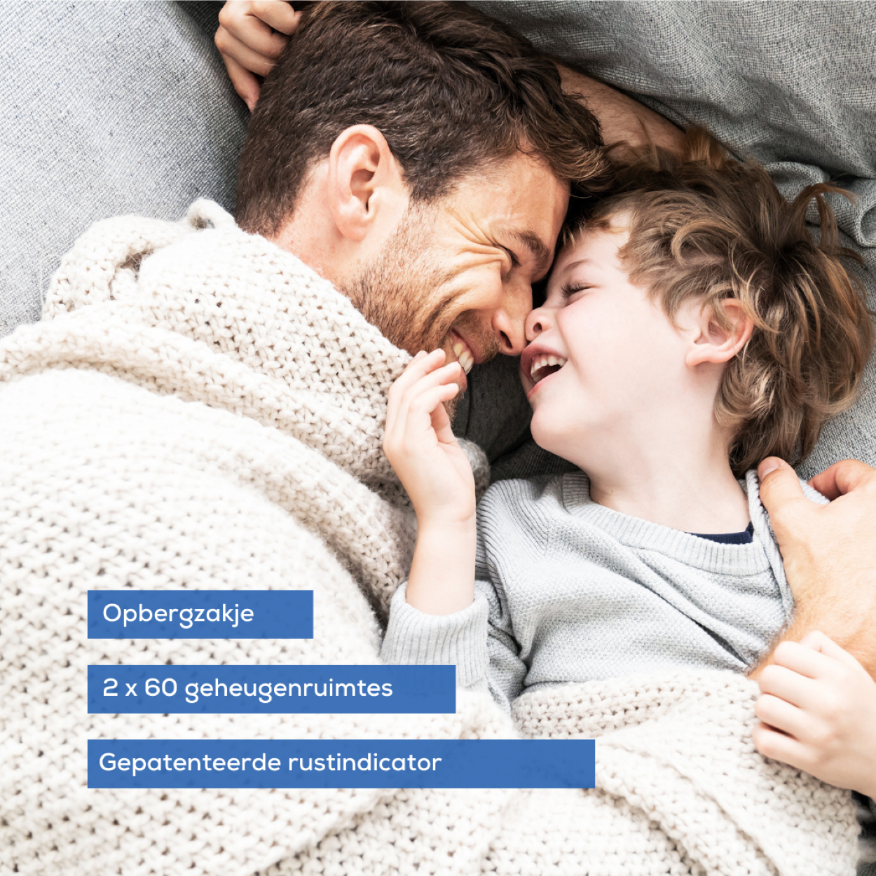 Ein Vater und sein Sohn liegen unter einer Decke und lächeln sich an.