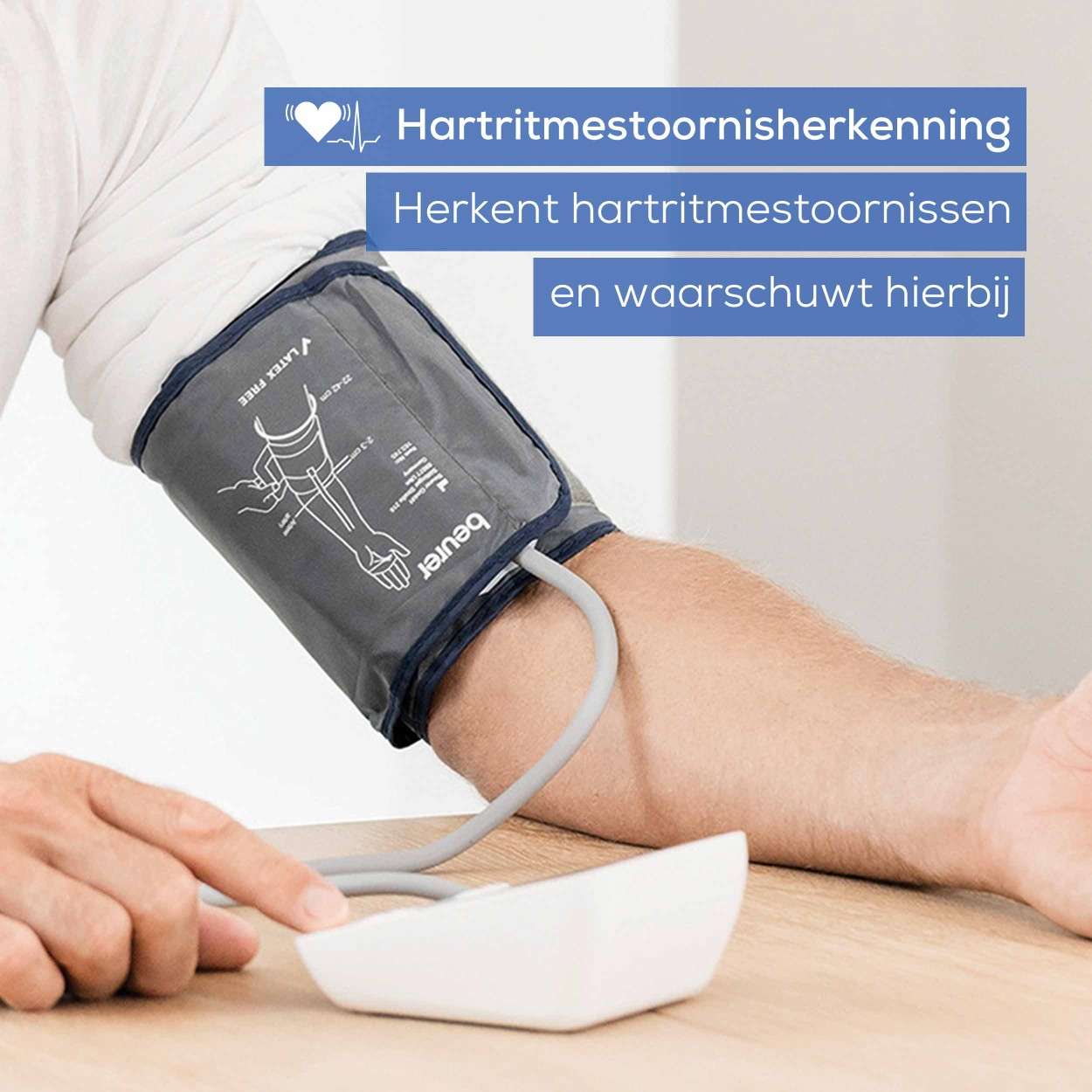 Person wearing a blood pressure cuff with a digital monitor, on a wooden table.