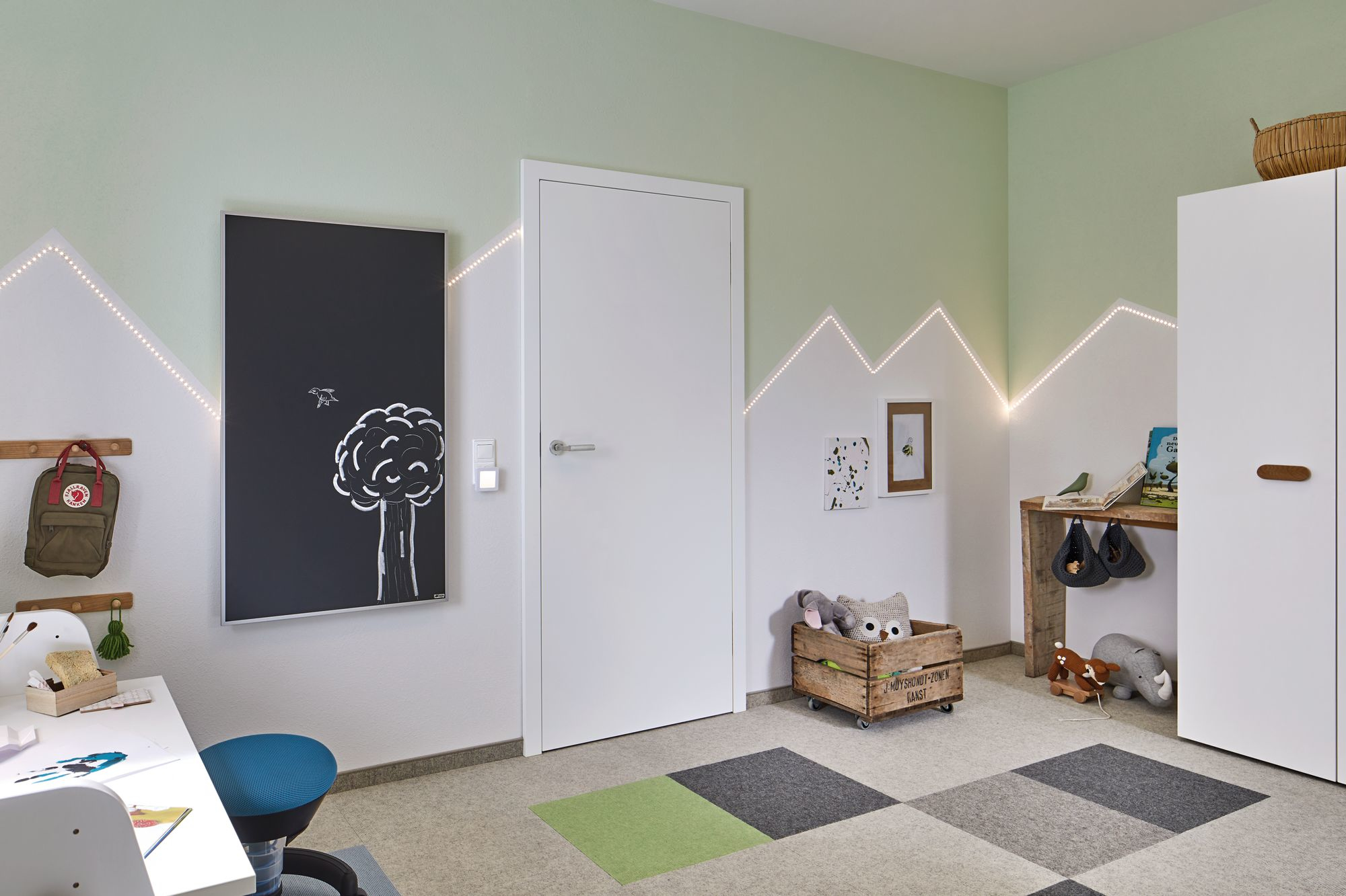 Ein Kinderzimmer mit grüner und weißer Farbgebung. Es gibt eine Tafel, eine Tür und eine Krippe.